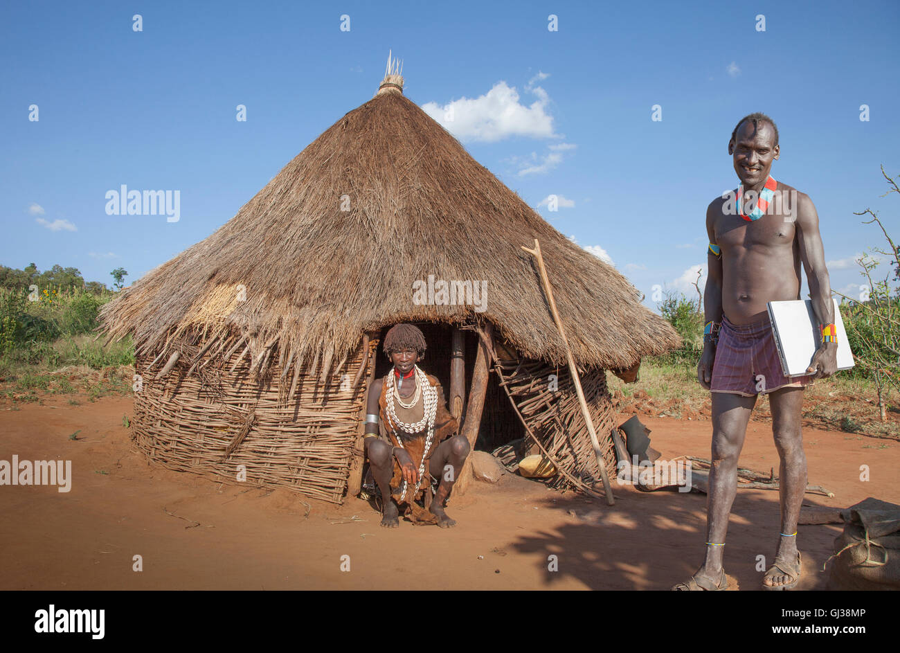 Man of the Karo tribe with laptop, while his wife in a hut is watching, Omo Valley, Ethiopia Stock Photo