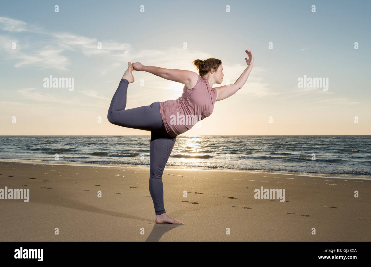 Mature woman practising yoga on a beach at sunset, tree pose Stock Photo