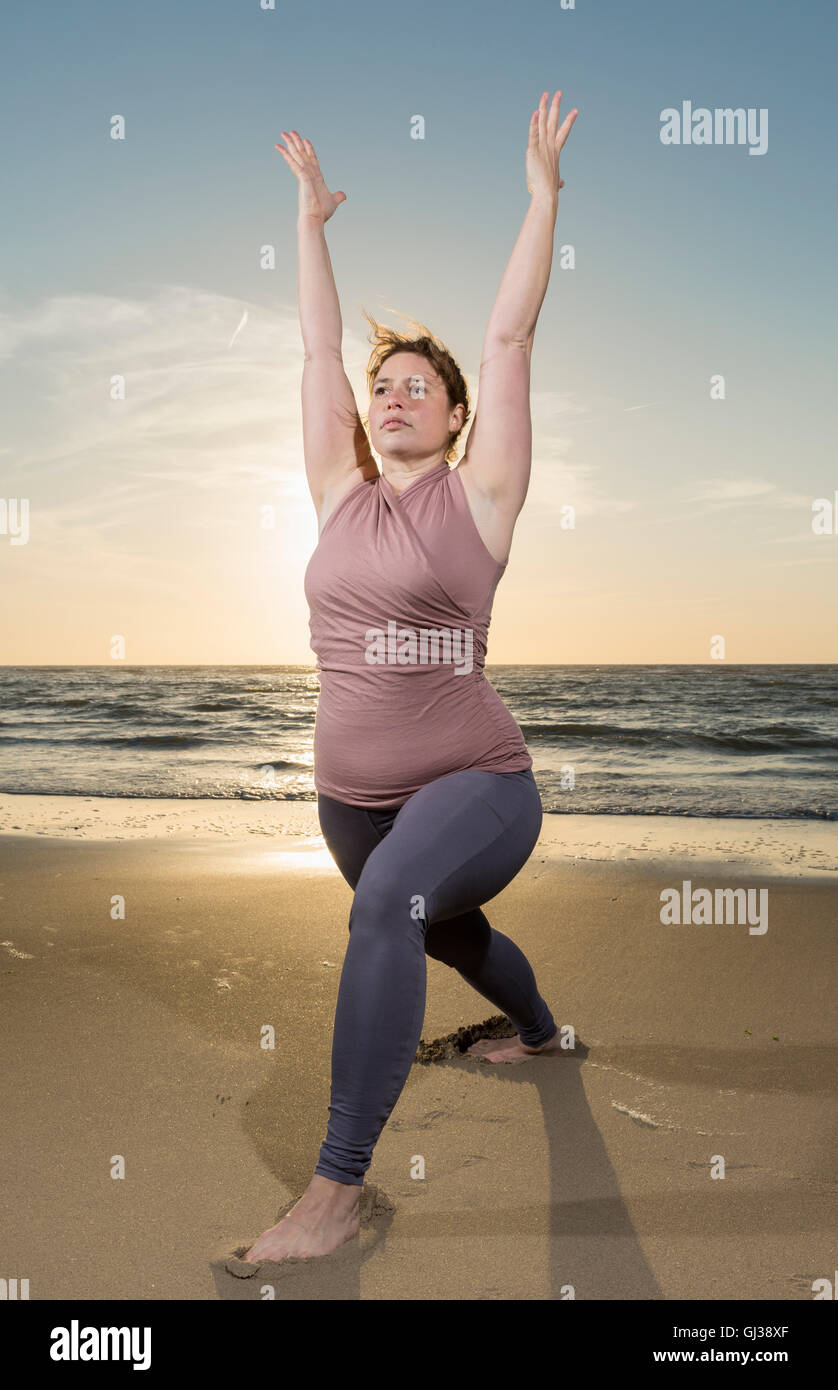 Mature woman practising yoga on a beach at sunset, warrior pose Stock Photo