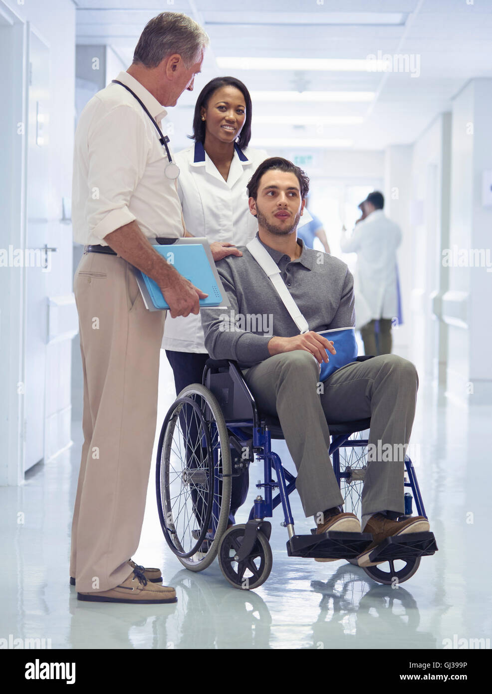 Doctor consulting with man in wheelchair with arm sling Stock Photo