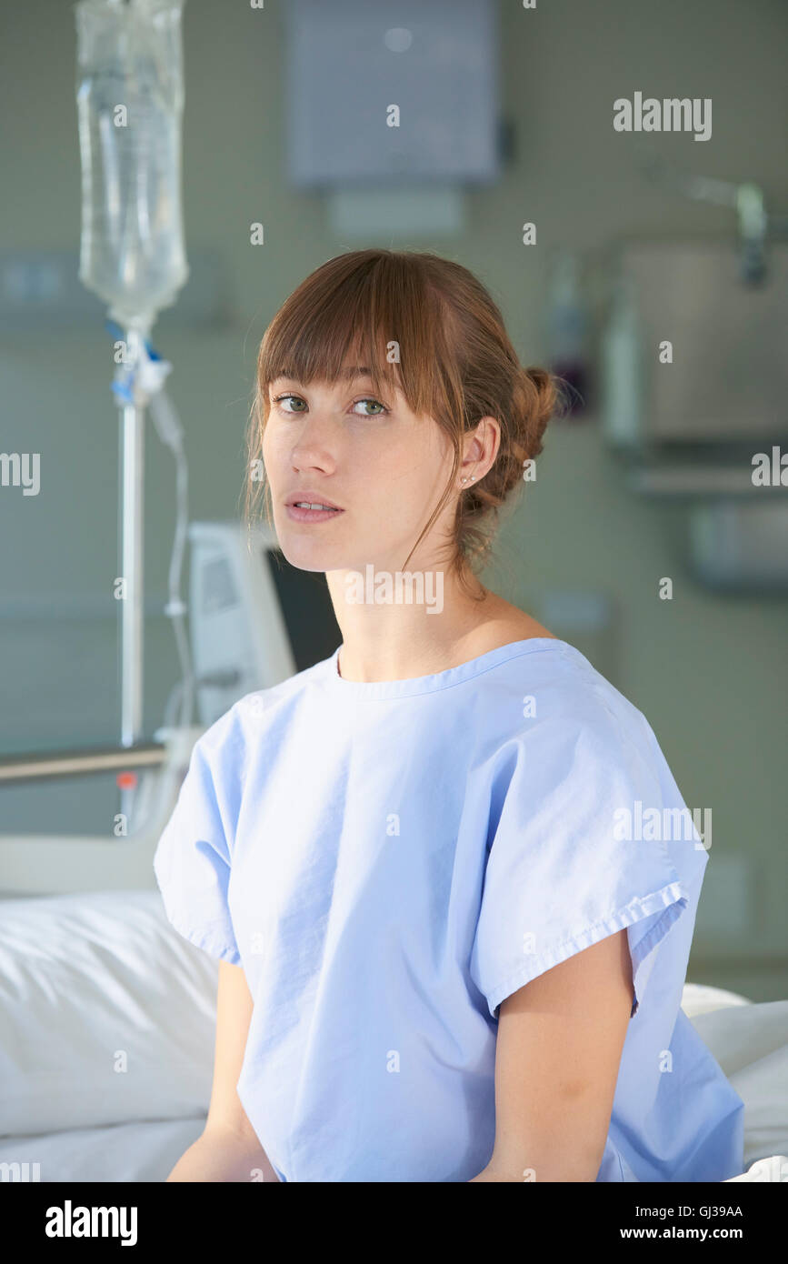 Woman sitting on hospital bed wearing hospital gown Stock Photo
