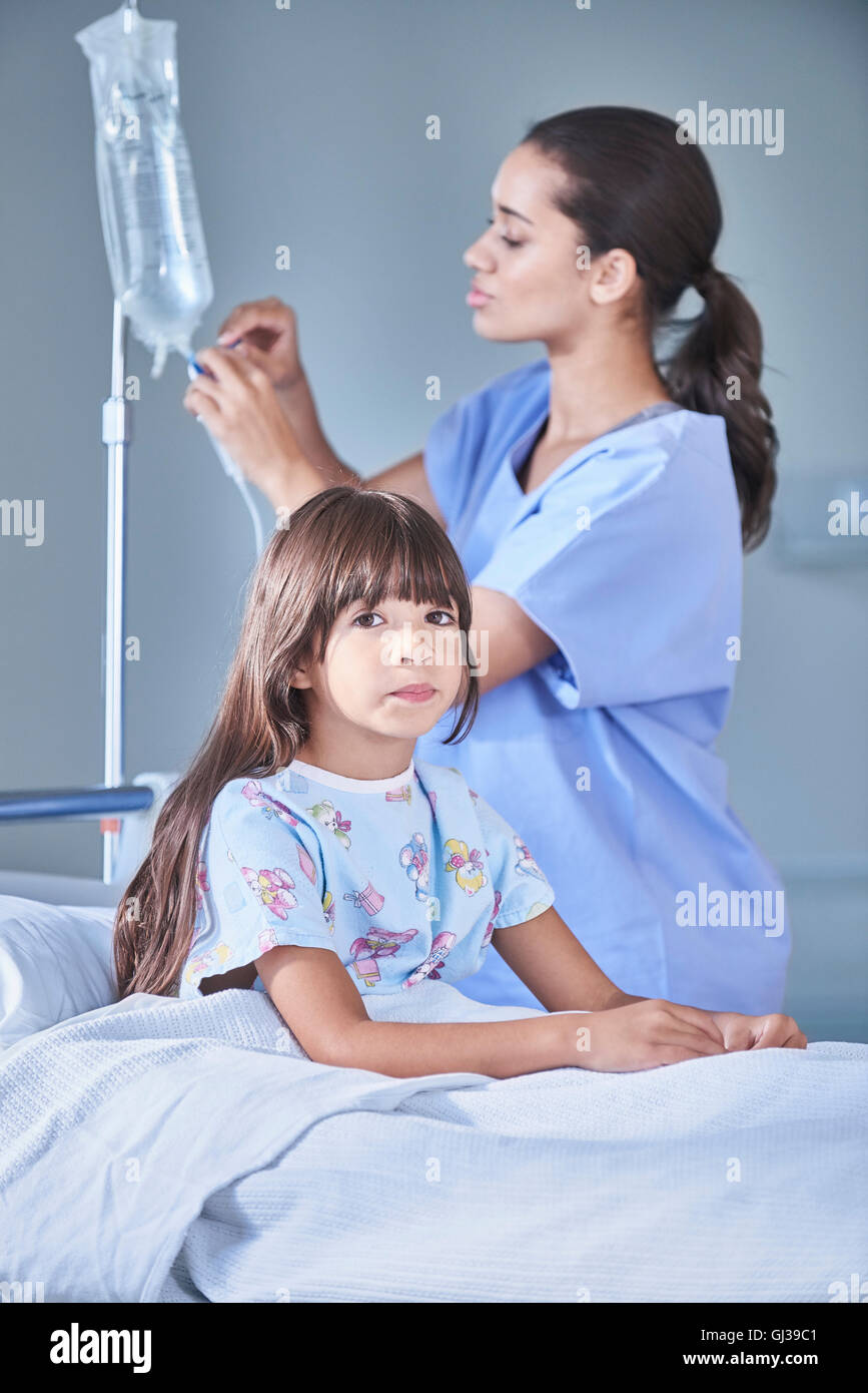 Female nurse adjusting girl patients intravenous drip in hospital children's ward Stock Photo