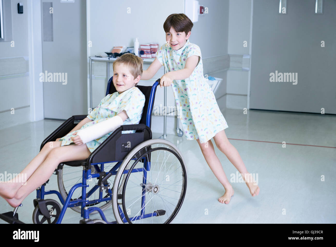 Boy patients pushing friend in wheelchair  on hospital children's ward Stock Photo