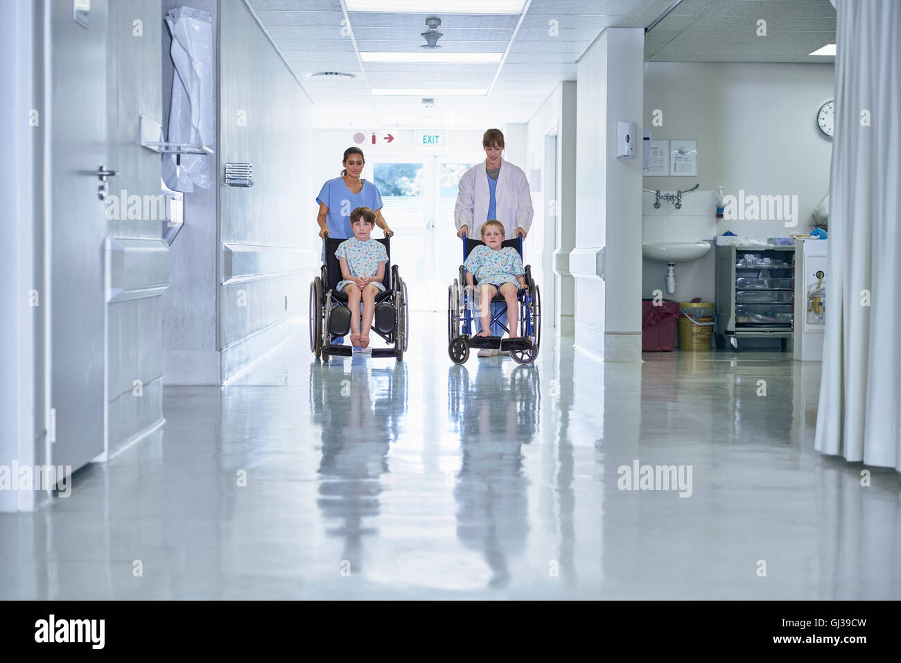 Medical orderly pushing boy patients in wheelchair  on hospital children's ward Stock Photo