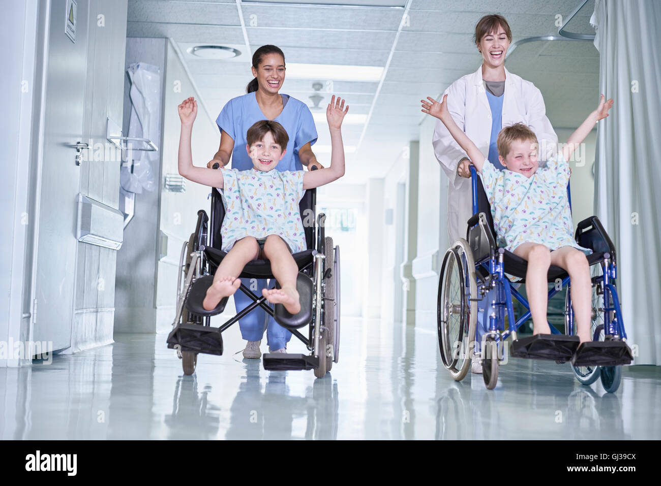 Medical orderlies having fun pushing boy patients in wheelchair  on hospital children's ward Stock Photo