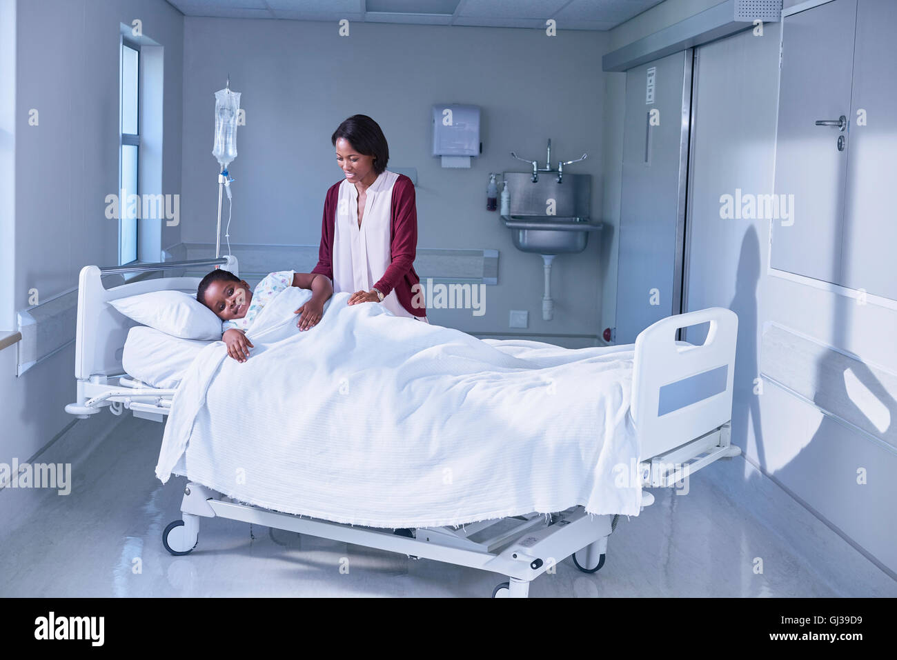 Girl patient in bed tended by her mother on hospital children's ward Stock Photo