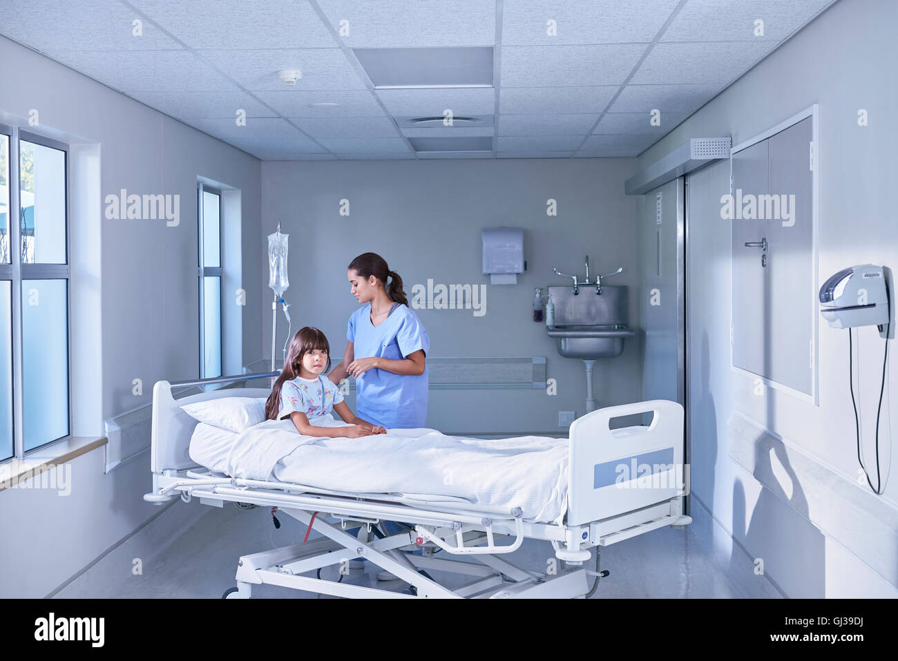 Nurse adjusting intravenous drip for girl patient in bed on hospital children's ward Stock Photo