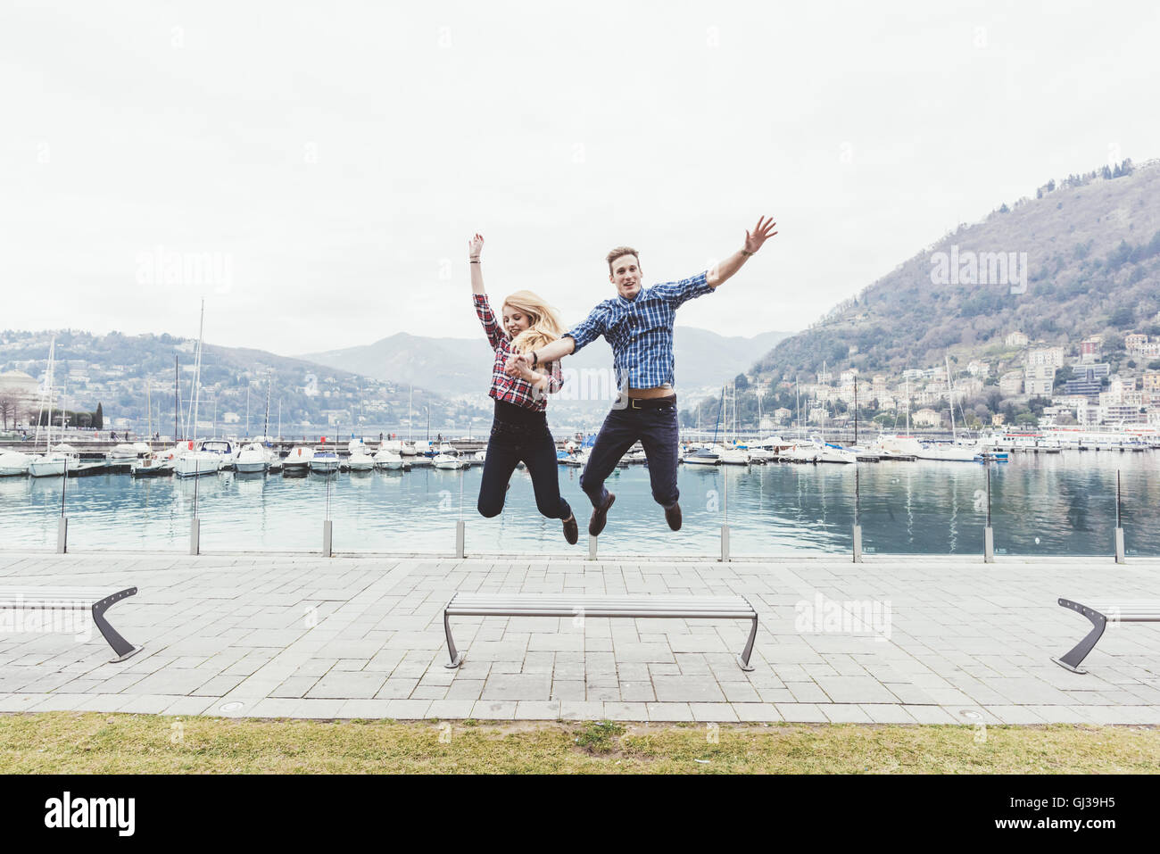 Young couple on waterfront jumping mid air,  Lake Como, Italy Stock Photo