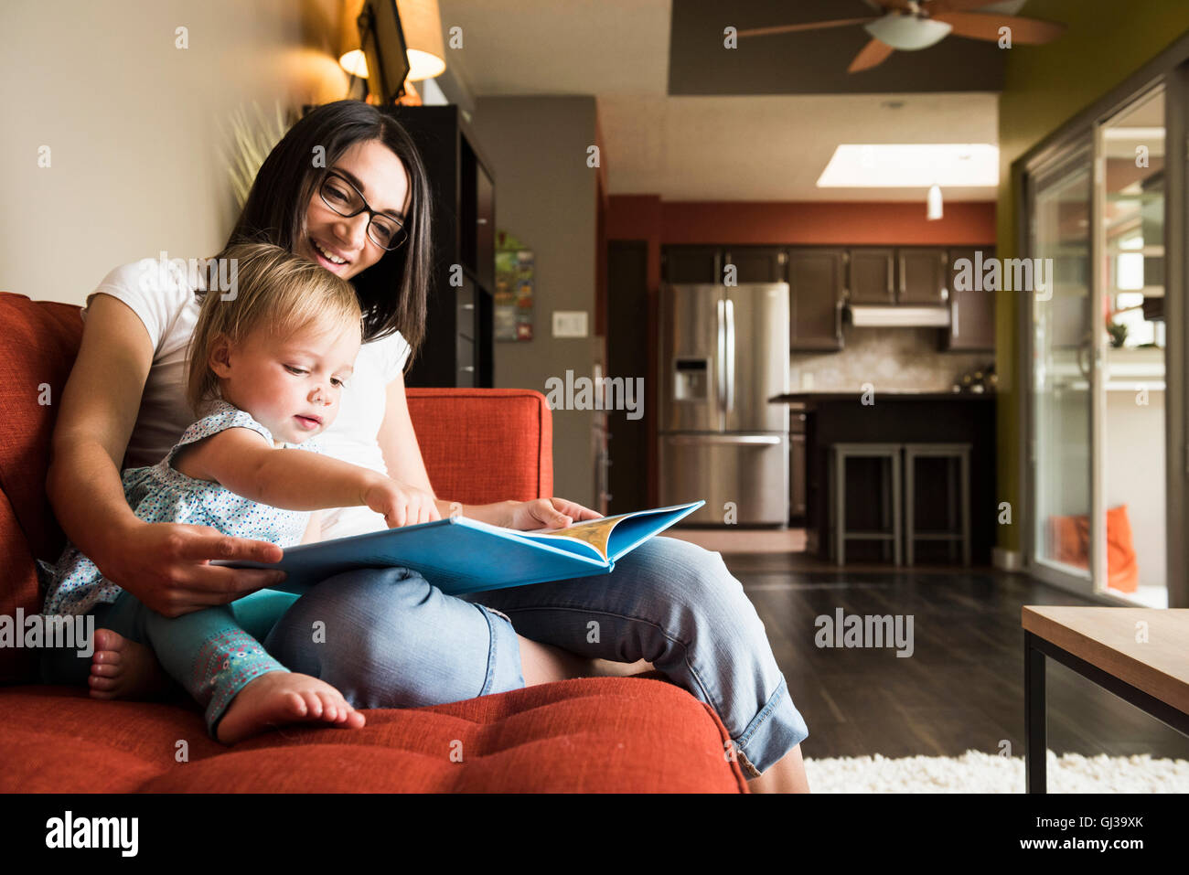 Mother teaching daughter to read book on sofa Stock Photo