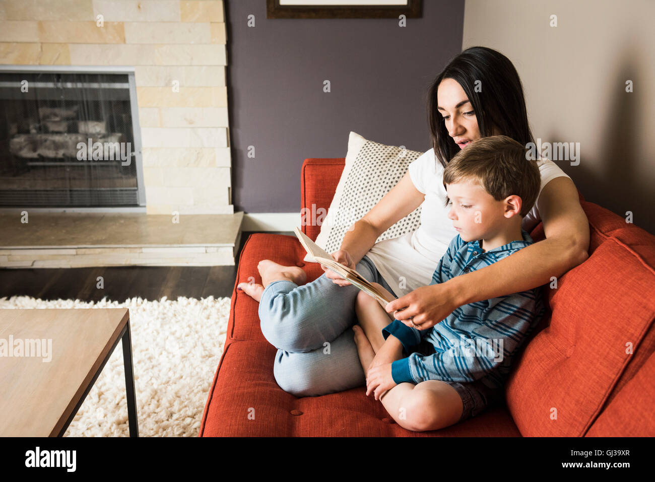 Mother teaching son to read book on sofa Stock Photo