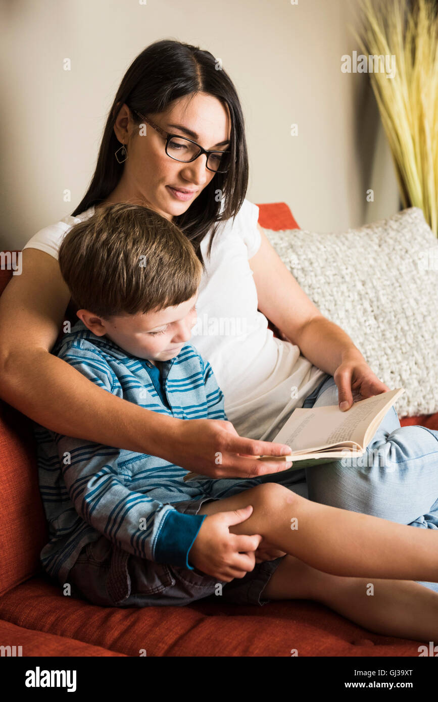 Mother teaching son to read book on sofa Stock Photo