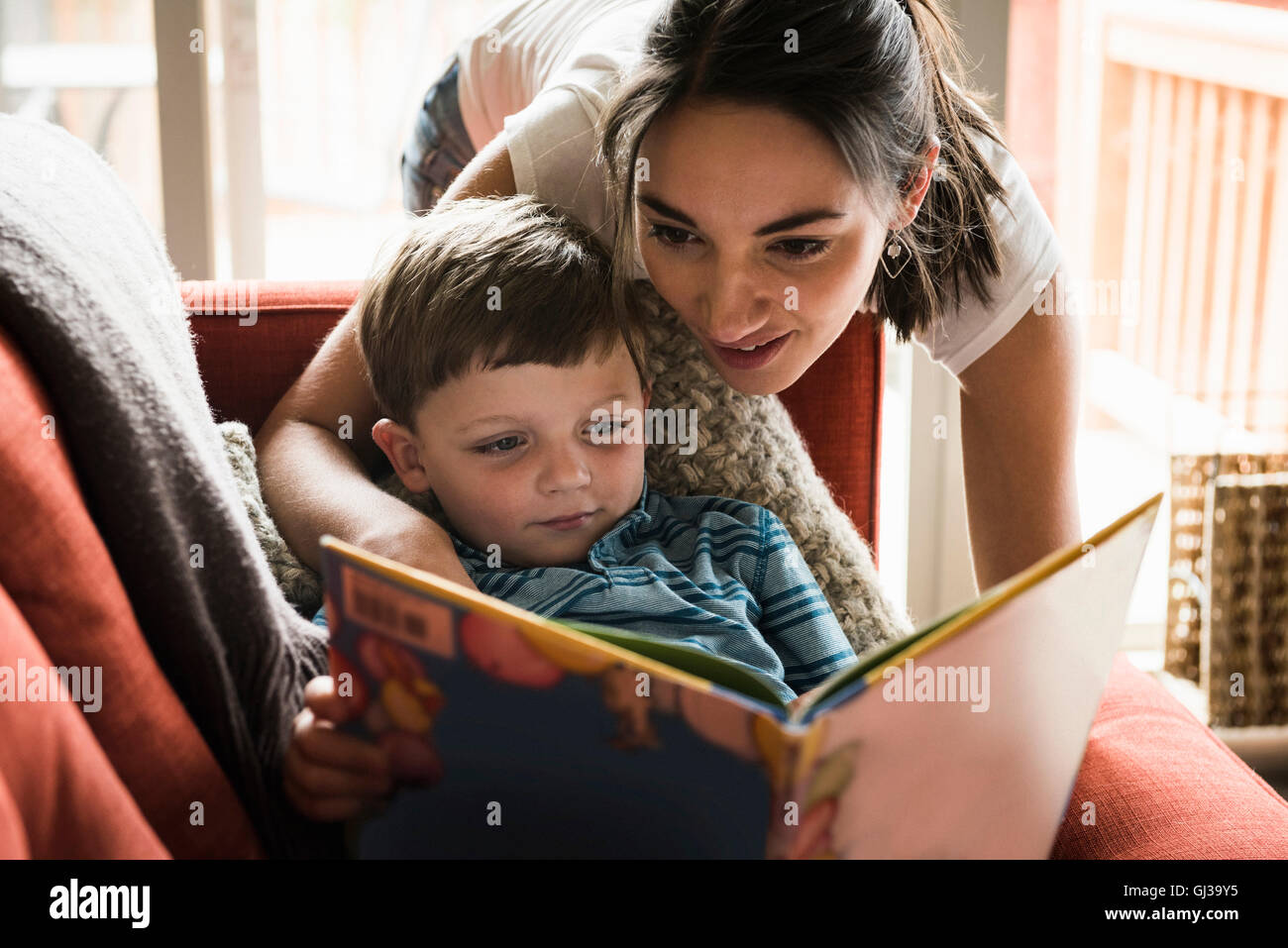 Mother teaching son to read book on sofa Stock Photo