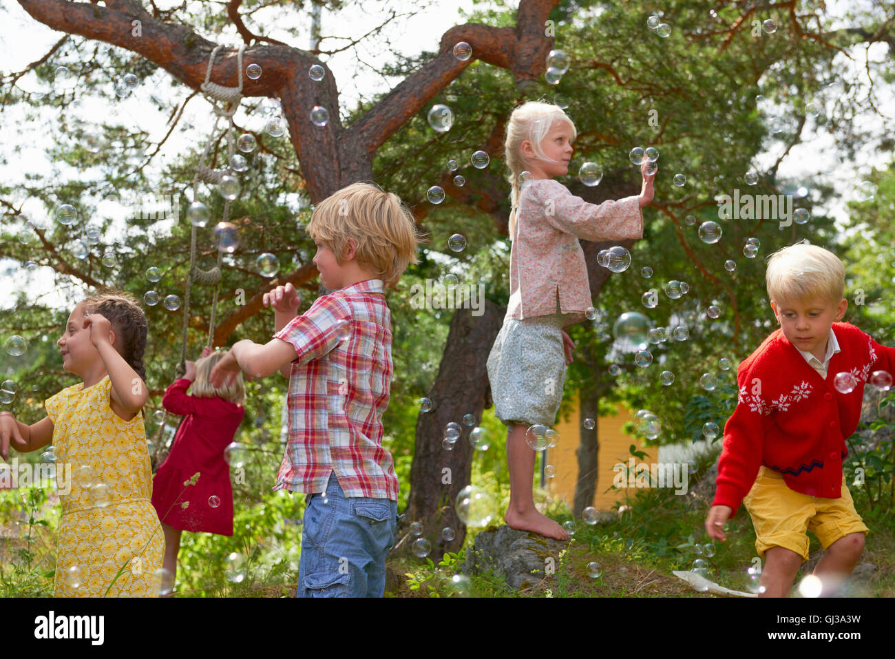 Group of young friends playing outdoors, reaching for bubbles Stock Photo