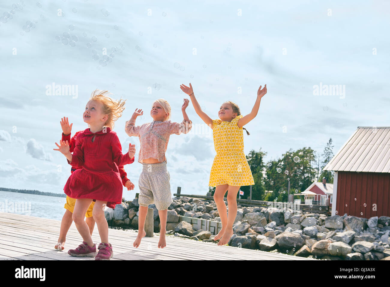 Group of young friends playing on wooden pier, reaching for bubbles Stock Photo