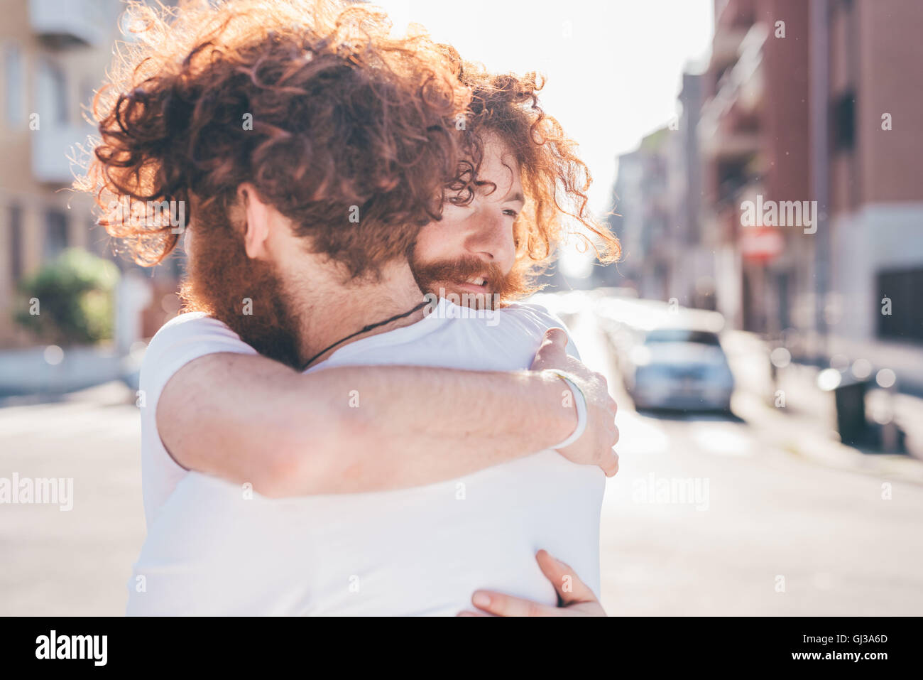 Young male hipster twins with red hair and beards hugging on city street Stock Photo