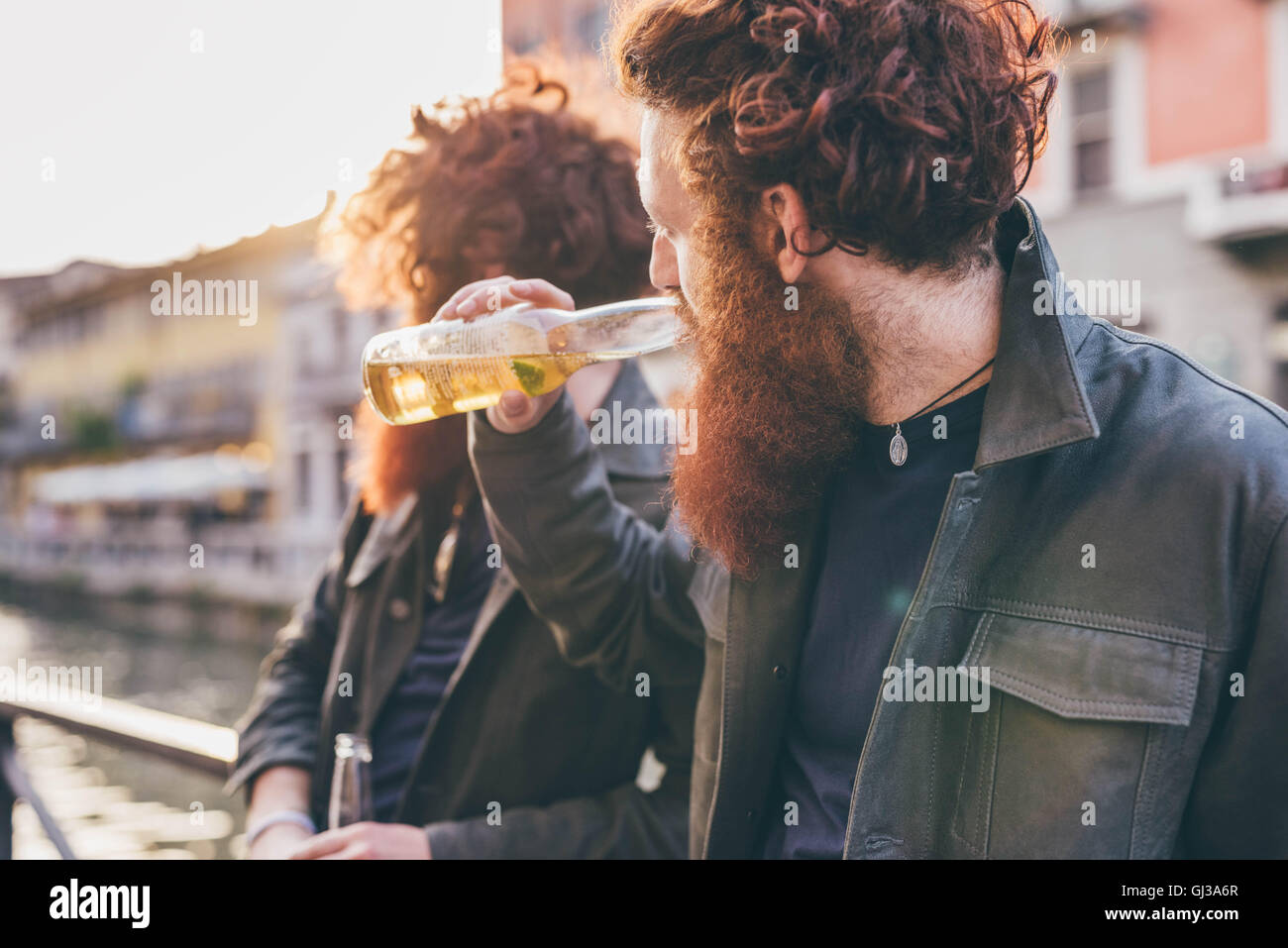 Young male hipster twins with red hair and beards drinking beer on canal waterfront Stock Photo