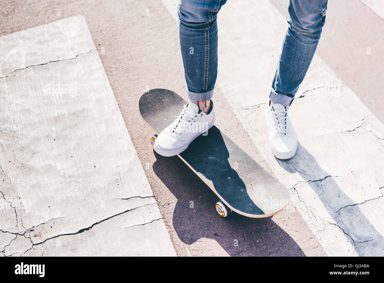 Legs and feet of young male skateboarder on pedestrian crossing Stock Photo