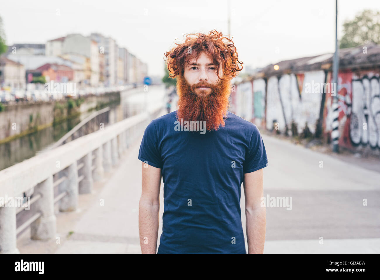 Close up portrait of young male hipster with red hair and beard standing on bridge Stock Photo