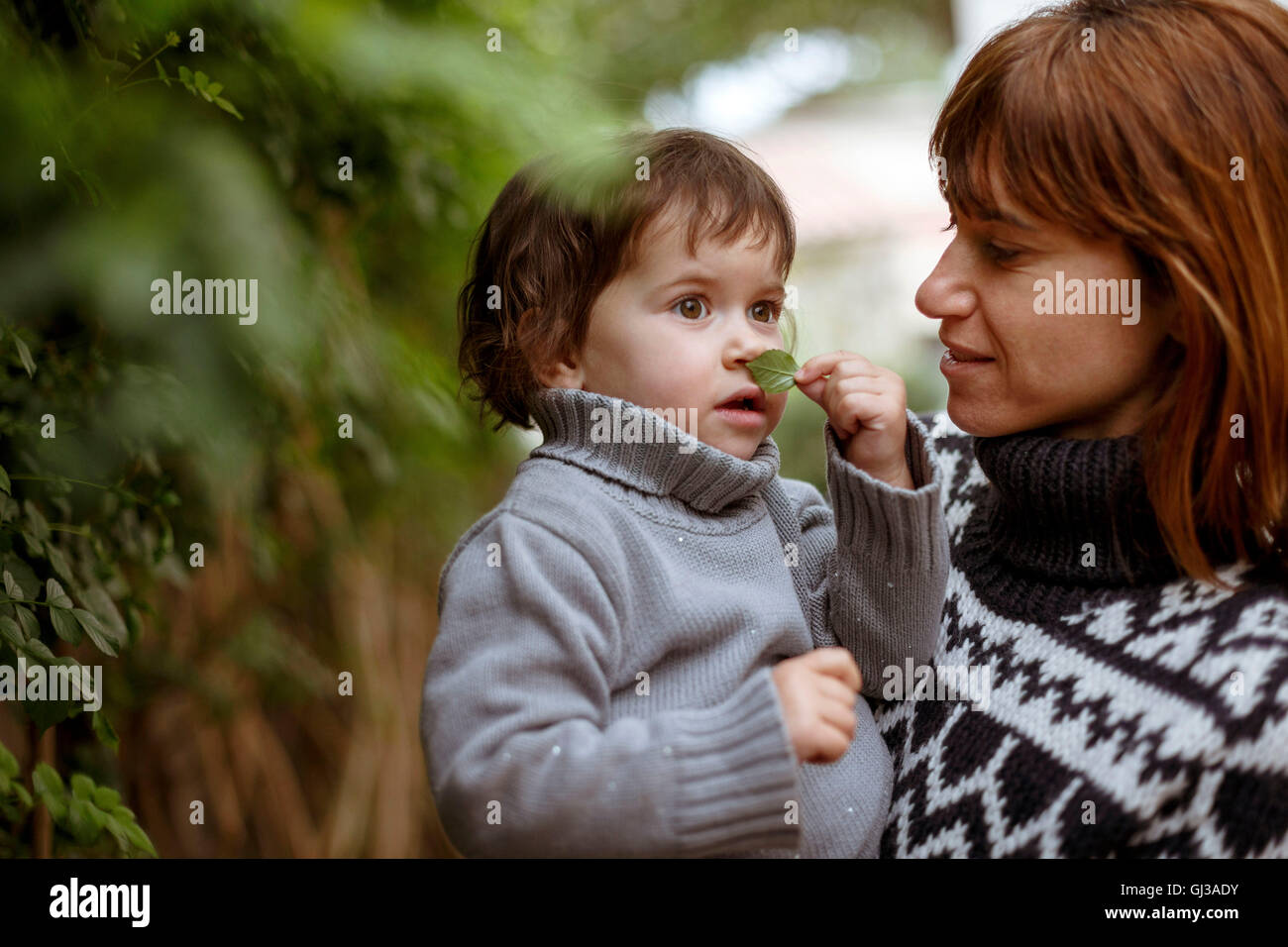 Mother holding daughter, smelling leaf Stock Photo