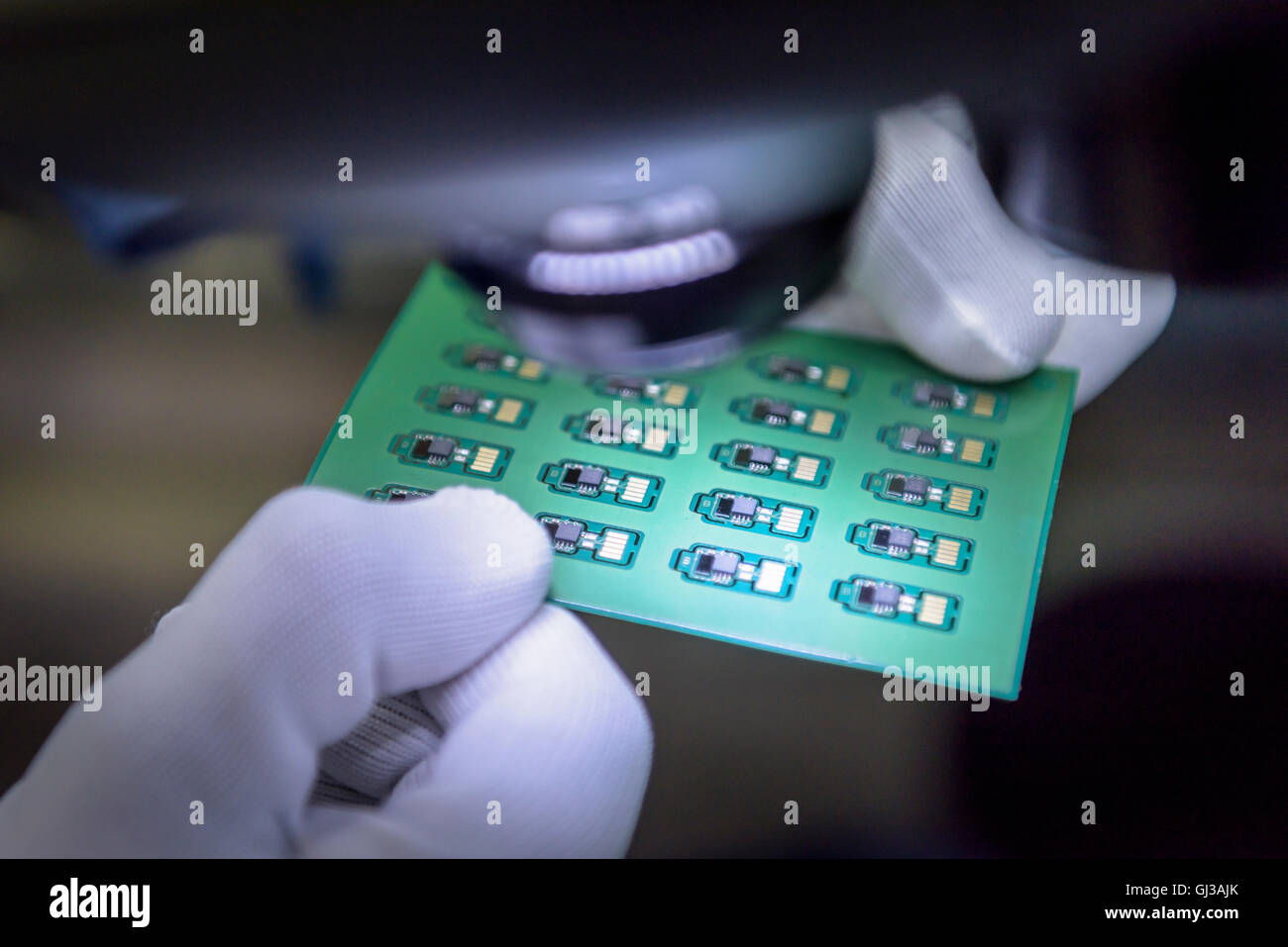 Worker inspecting circuit boards under microscope in circuit board