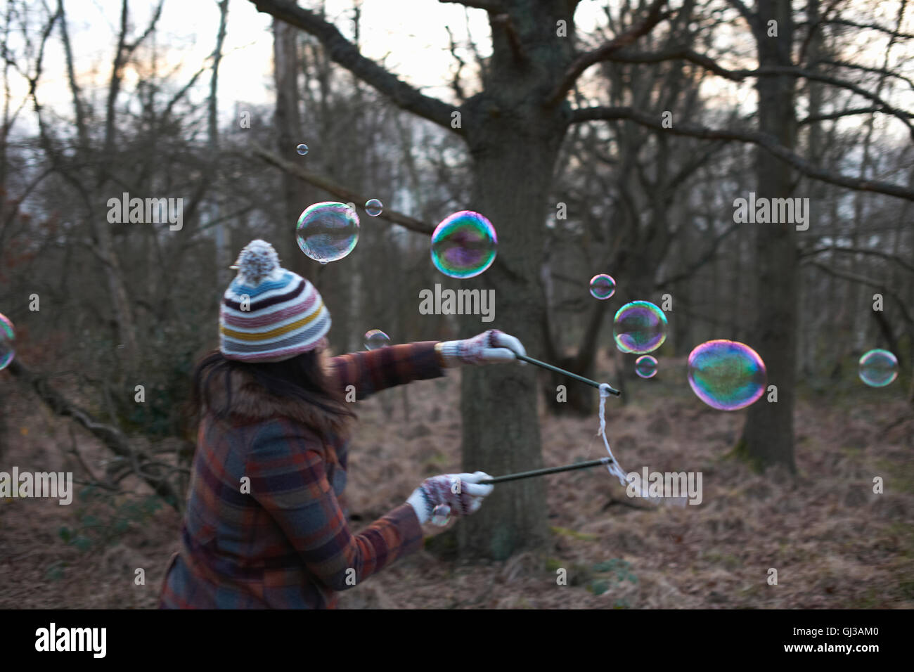 Woman in forest using bubble wands to make bubbles Stock Photo