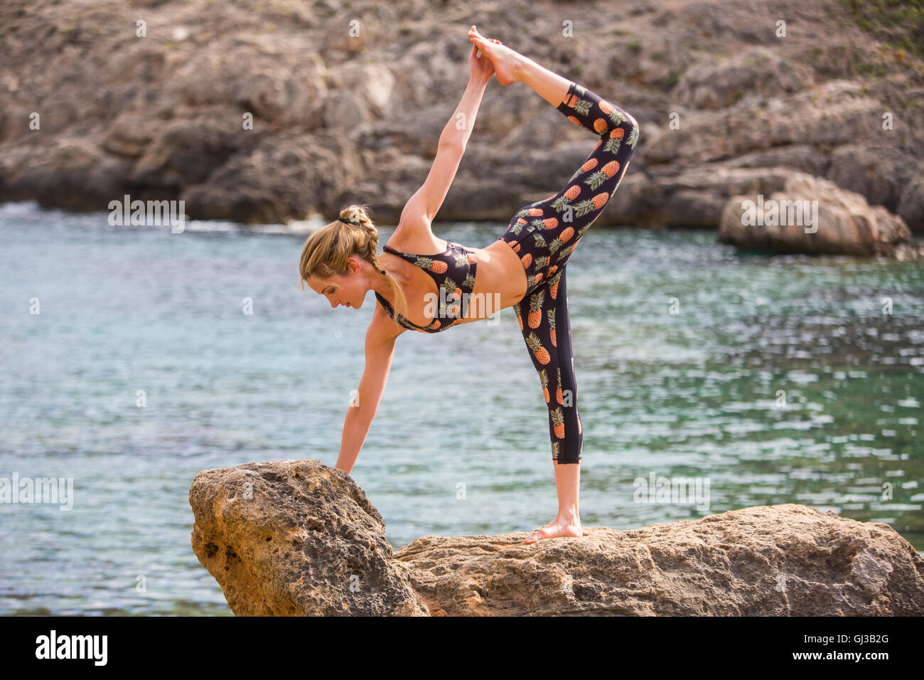 Young woman practicing yoga position on sea rocks, Majorca, Spain Stock Photo