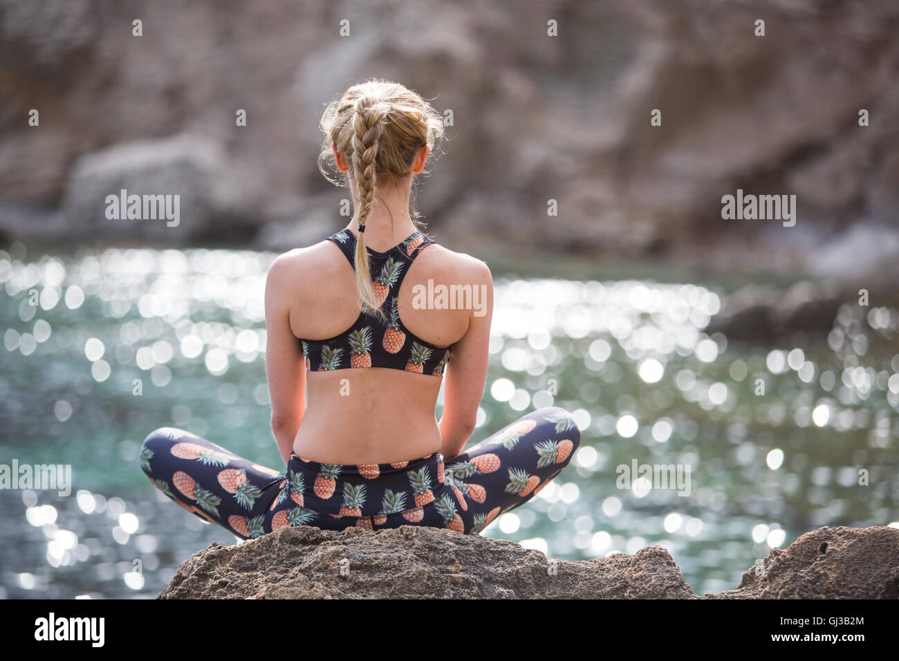 Rear view of young woman practicing yoga lotus position on sea rocks, Majorca, Spain Stock Photo