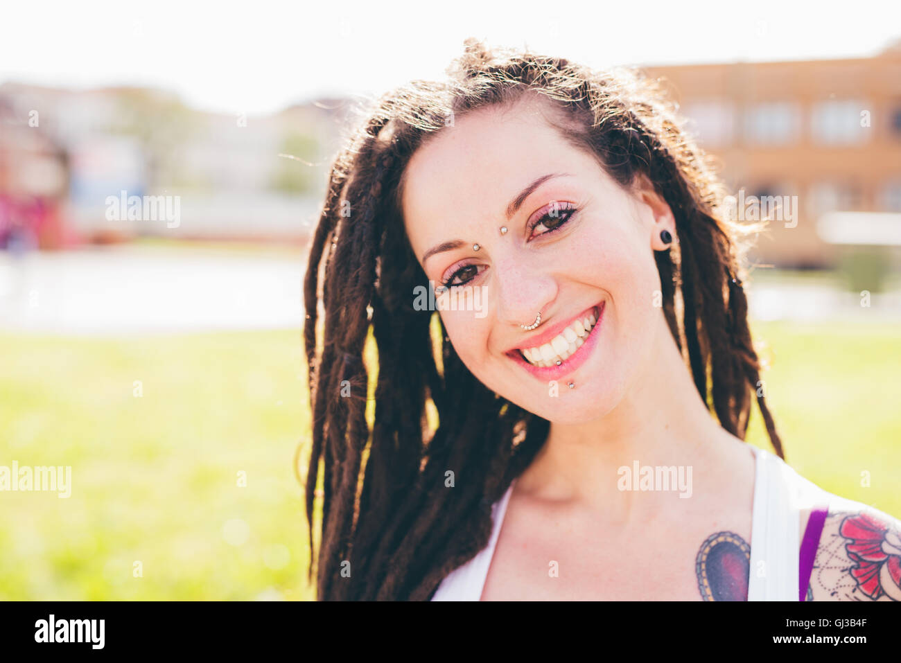 Portrait of tattooed young woman with dreadlocks in urban park Stock Photo