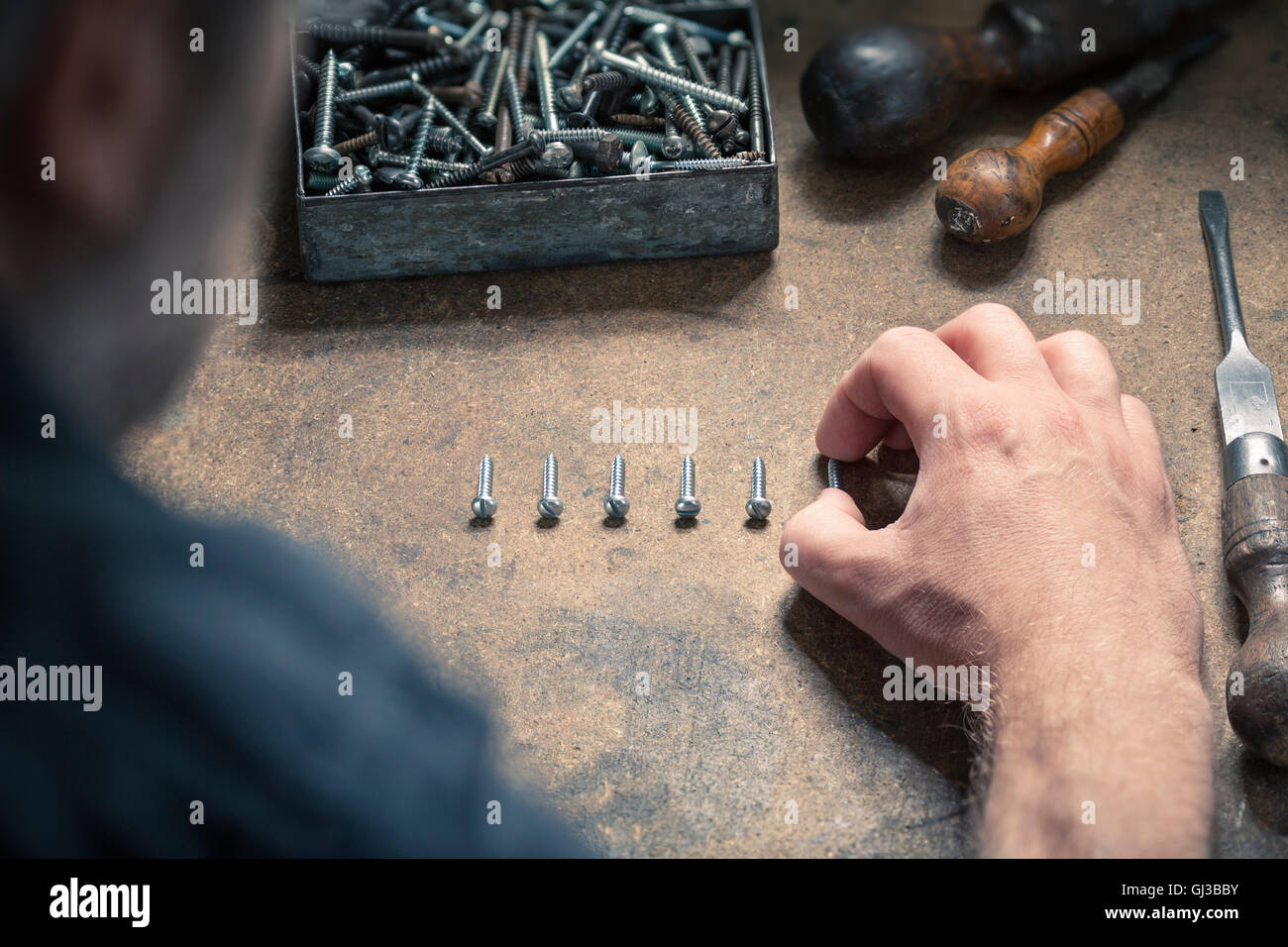 Man arranging screws of similar size in a row Stock Photo
