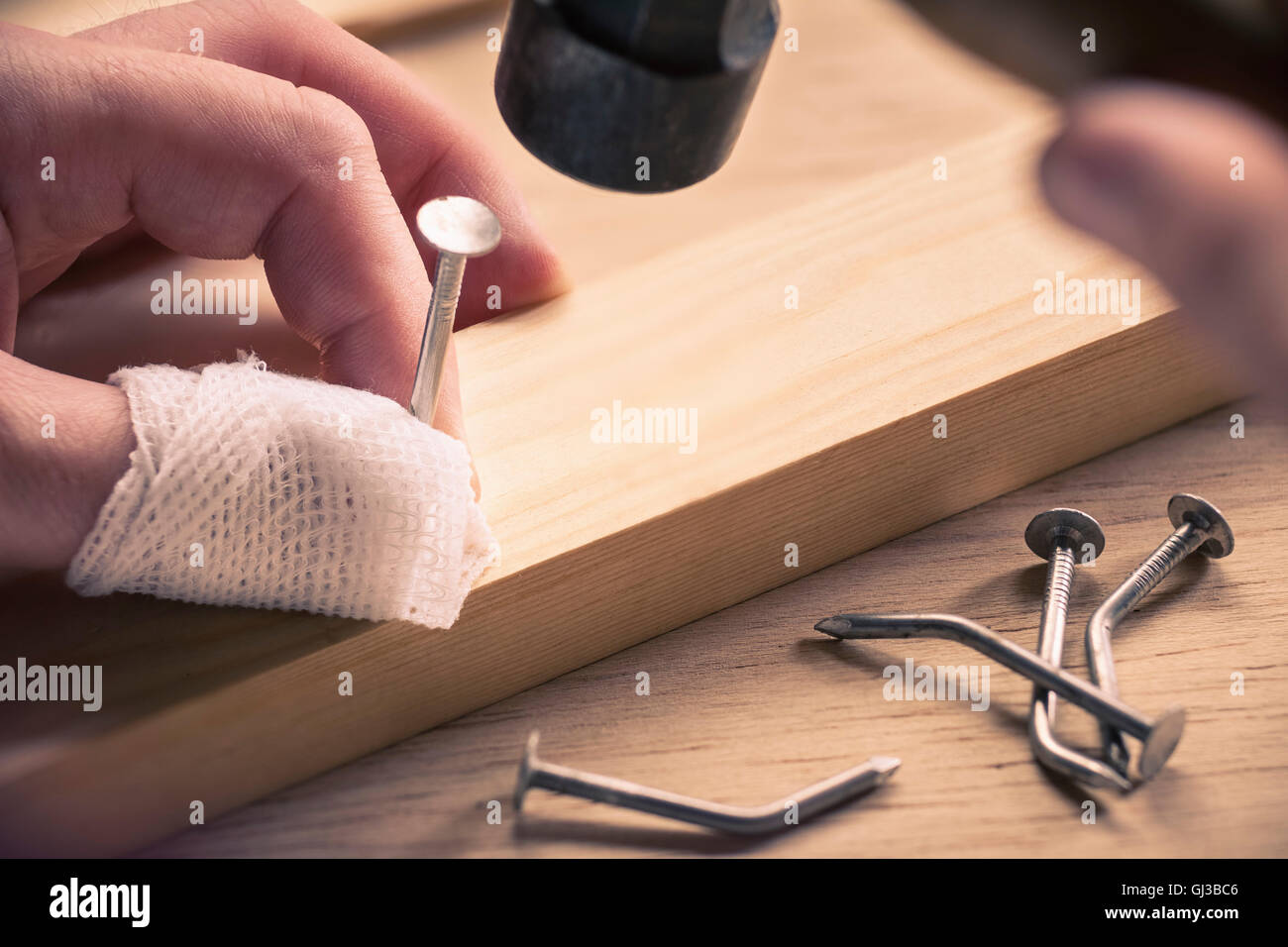 Bandaged finger holding nail on wood Stock Photo