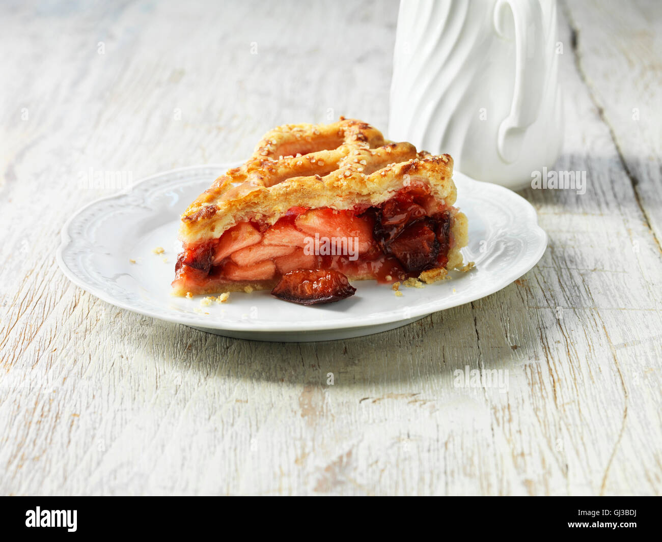 Apple, plum and raspberry pie on white plate, white jug, white washed wooden table Stock Photo