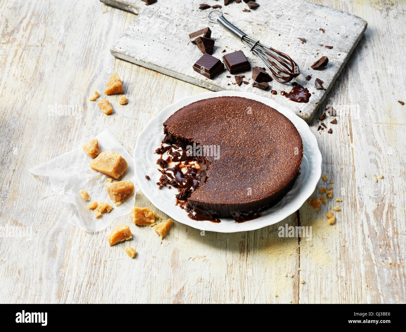Hot chocolate fudge pudding, crumbly fudge, pieces of chocolate, whisk, white washed wooden table and chopping board Stock Photo