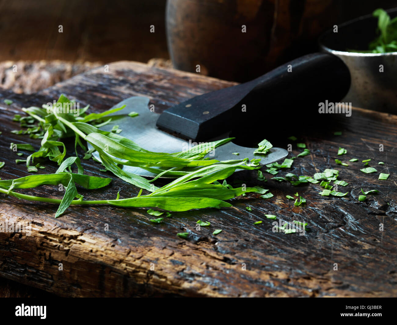 Tarragon, whole and chopped, mezzaluna on vintage chopping board Stock Photo