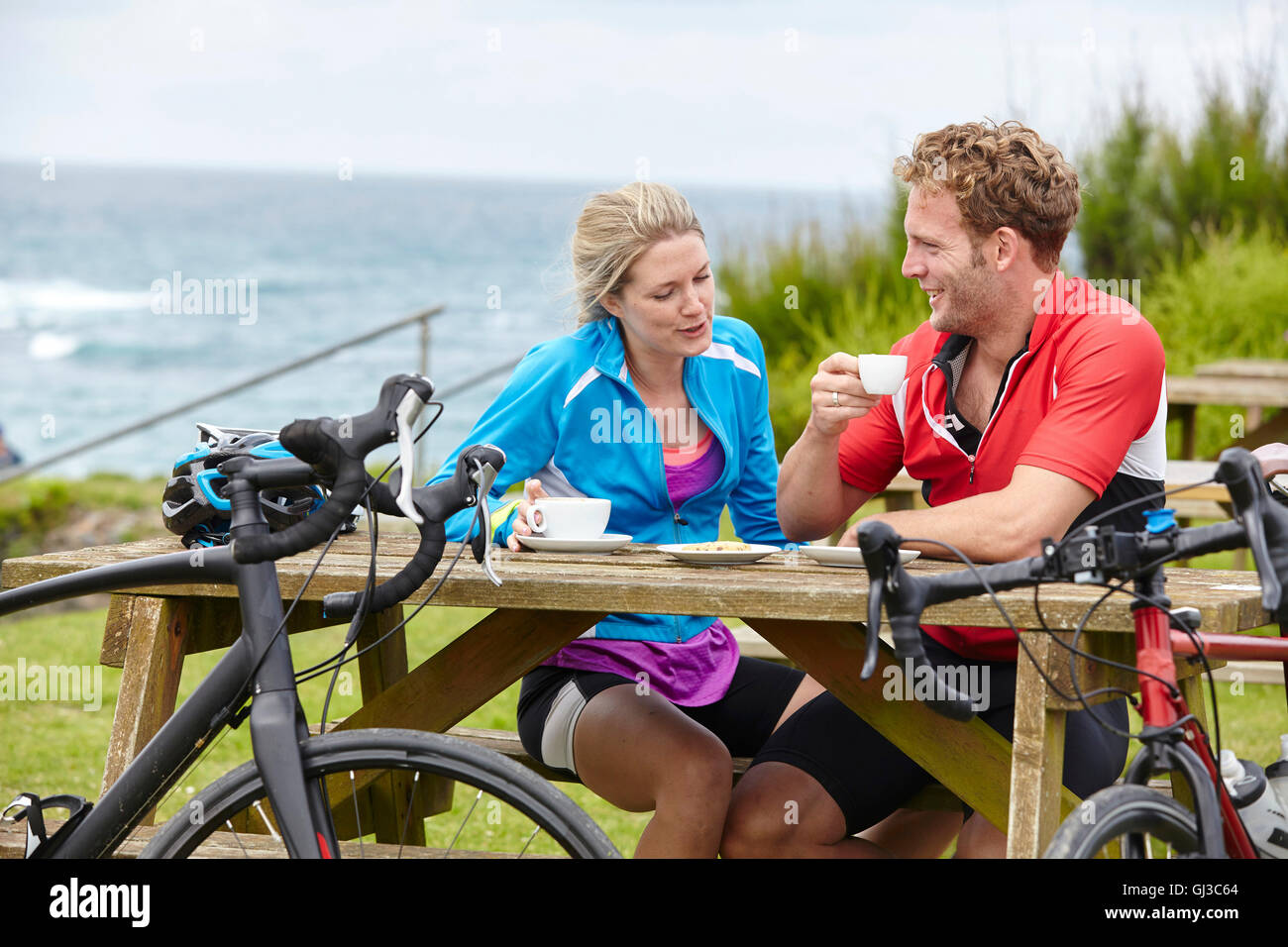 Cyclists relaxing at picnic table overlooking ocean Stock Photo