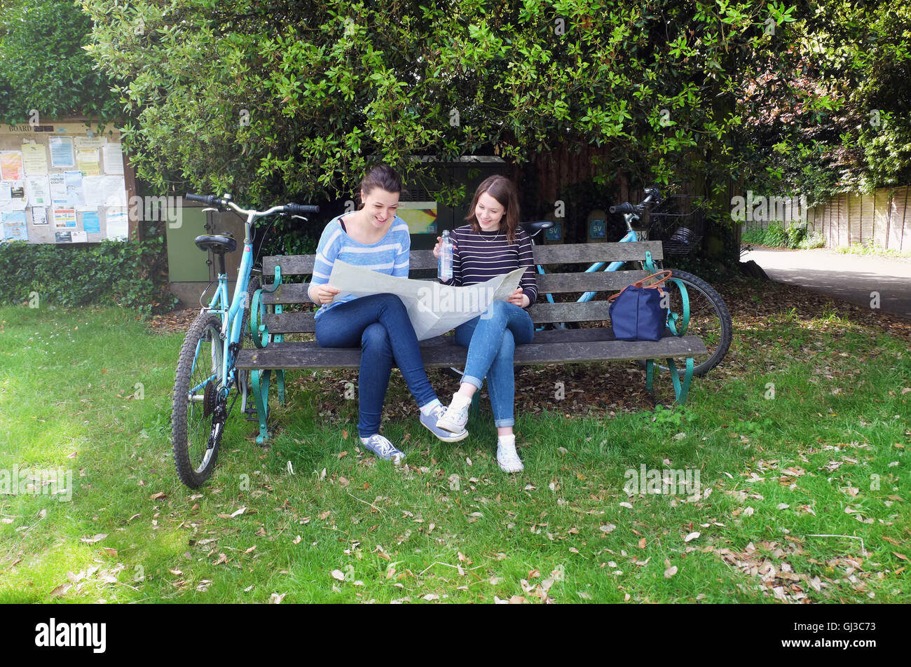 Young adult sisters with bicycles sitting on bench looking at map Stock Photo