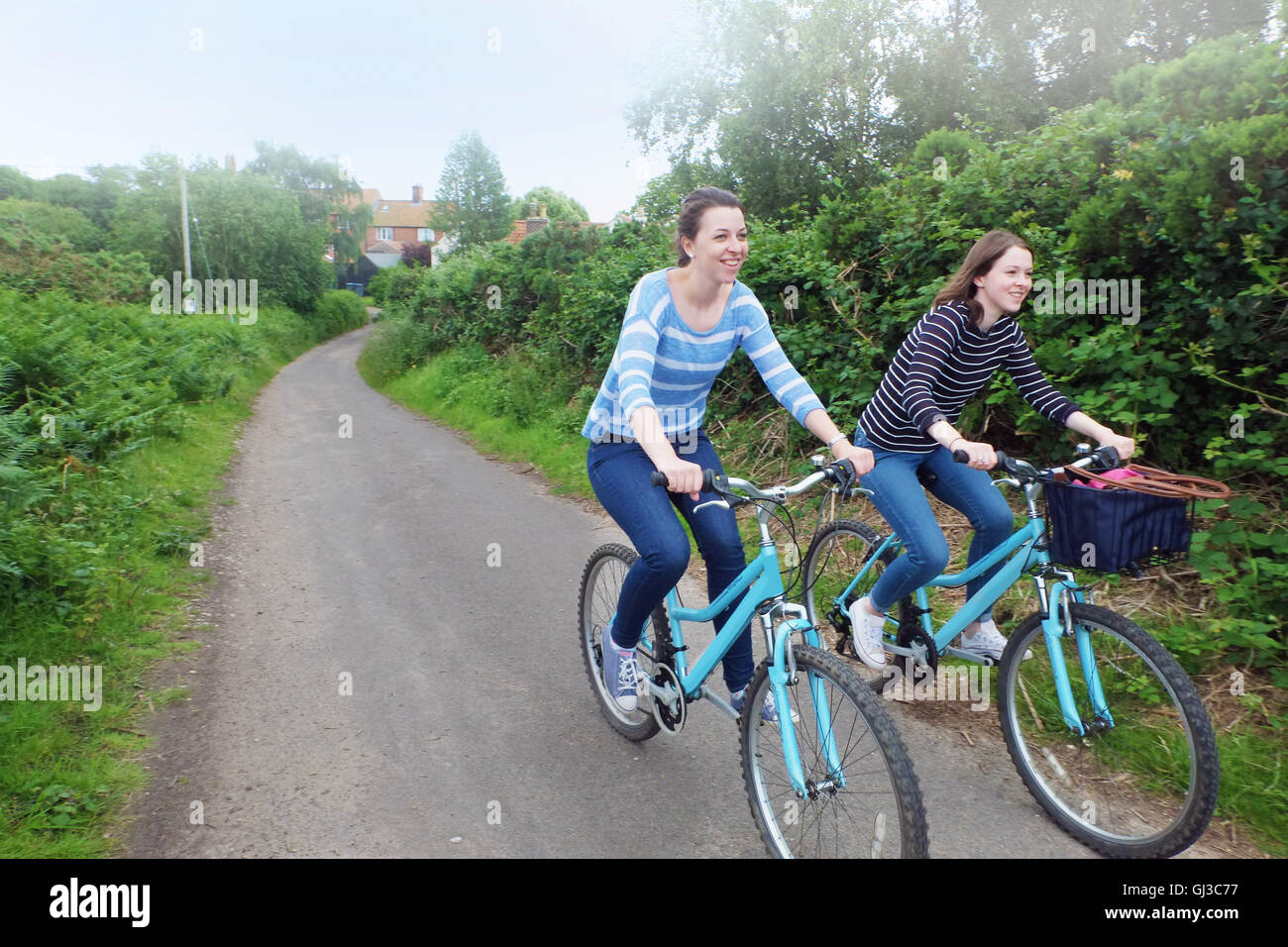 Two young adult sisters cycling along country lane Stock Photo