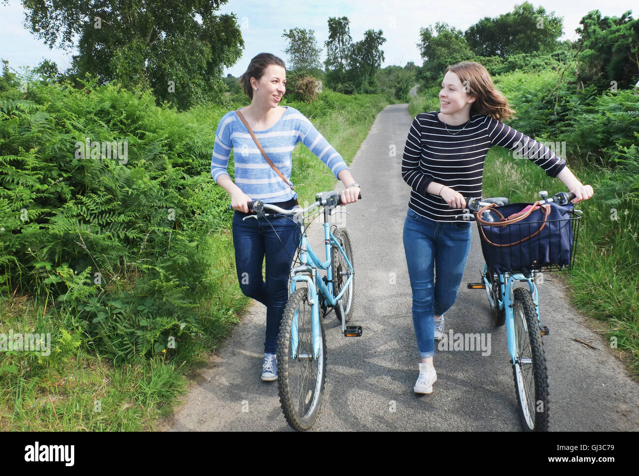 Two young adults pushing bicycles and chatting along country lane Stock Photo