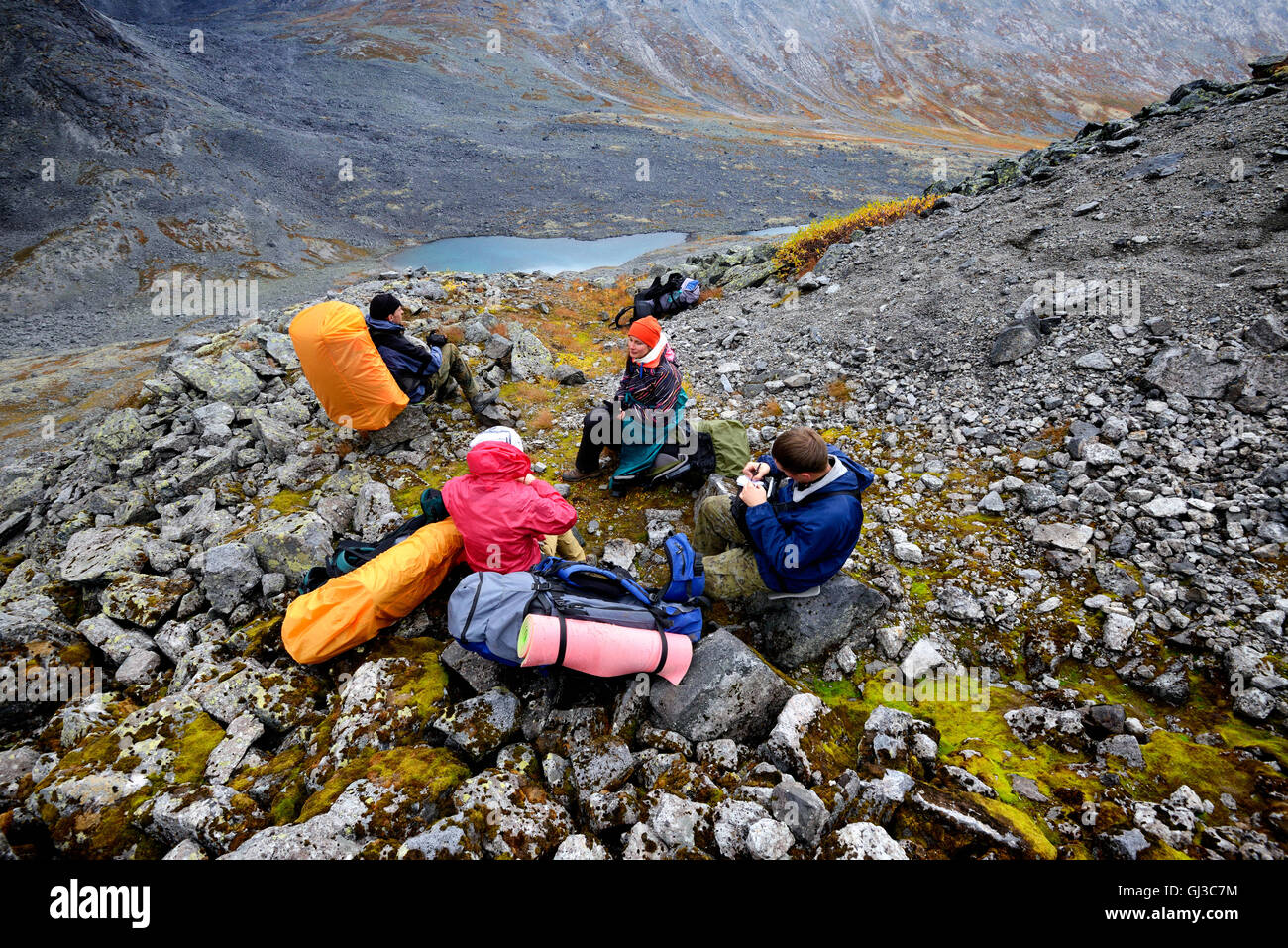 Four adult hikers taking a break in rugged valley landscape, Khibiny mountains, Kola Peninsula, Russia Stock Photo