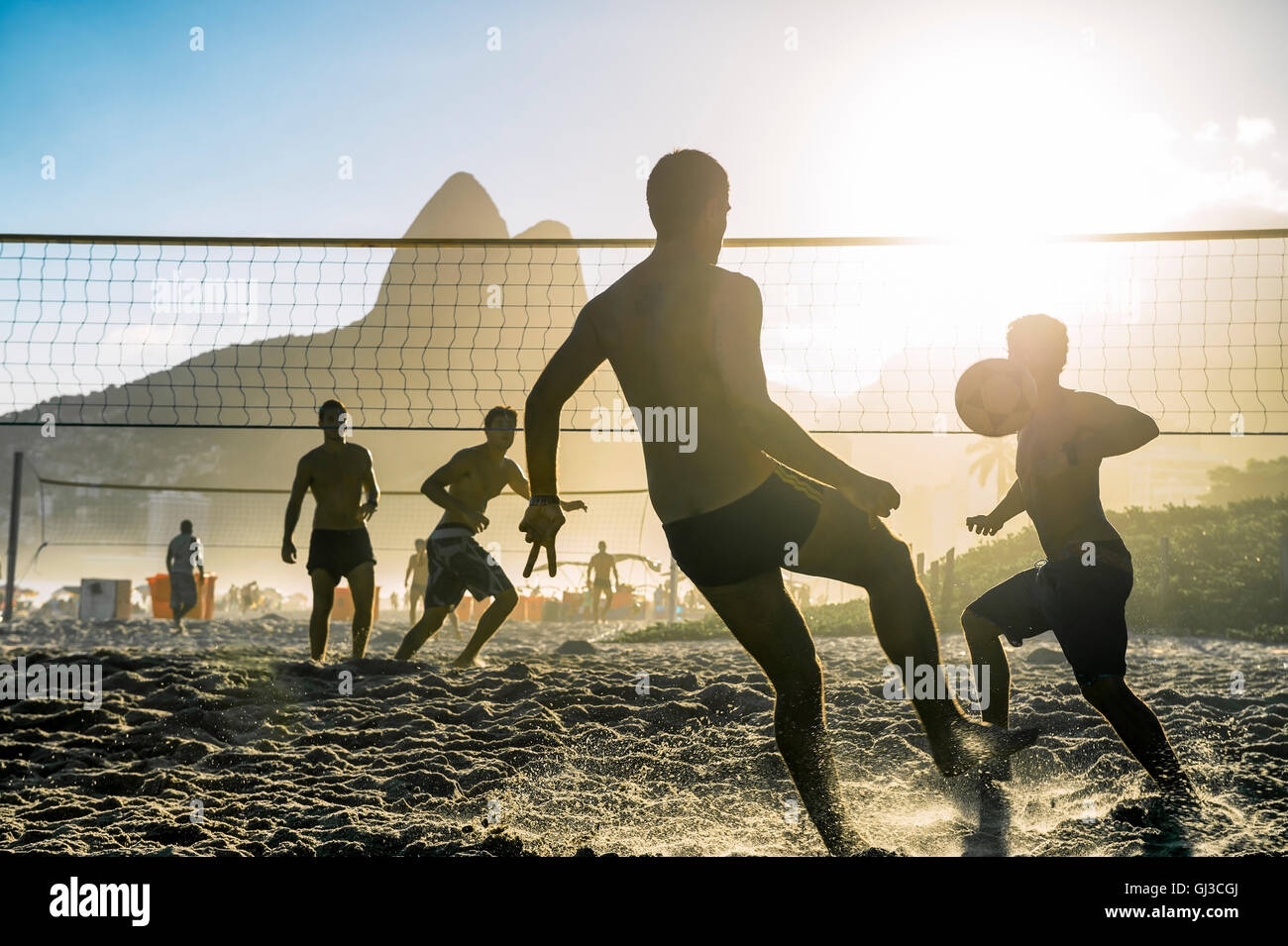 Silhouettes of carioca Brazilians playing futevolei (footvolley) against a sunset backdrop of Dois Irmaos Two Brothers Mountain Stock Photo
