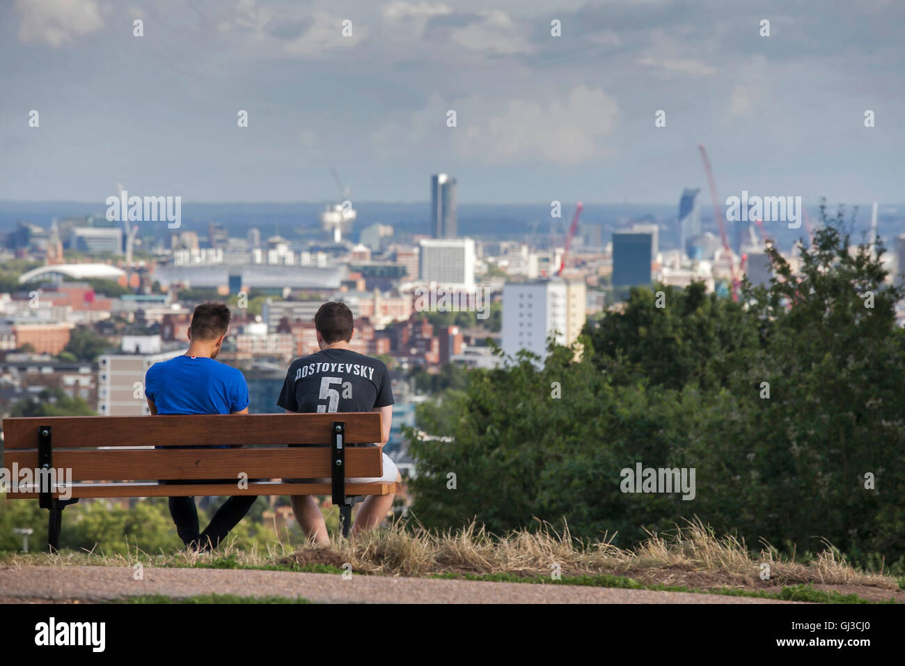 LONDON - MAY 10, 2015. Two men in T-shirt with "Dostoevsky" sign sitting on bench, admiring the view of London in Primrose Hill Stock Photo