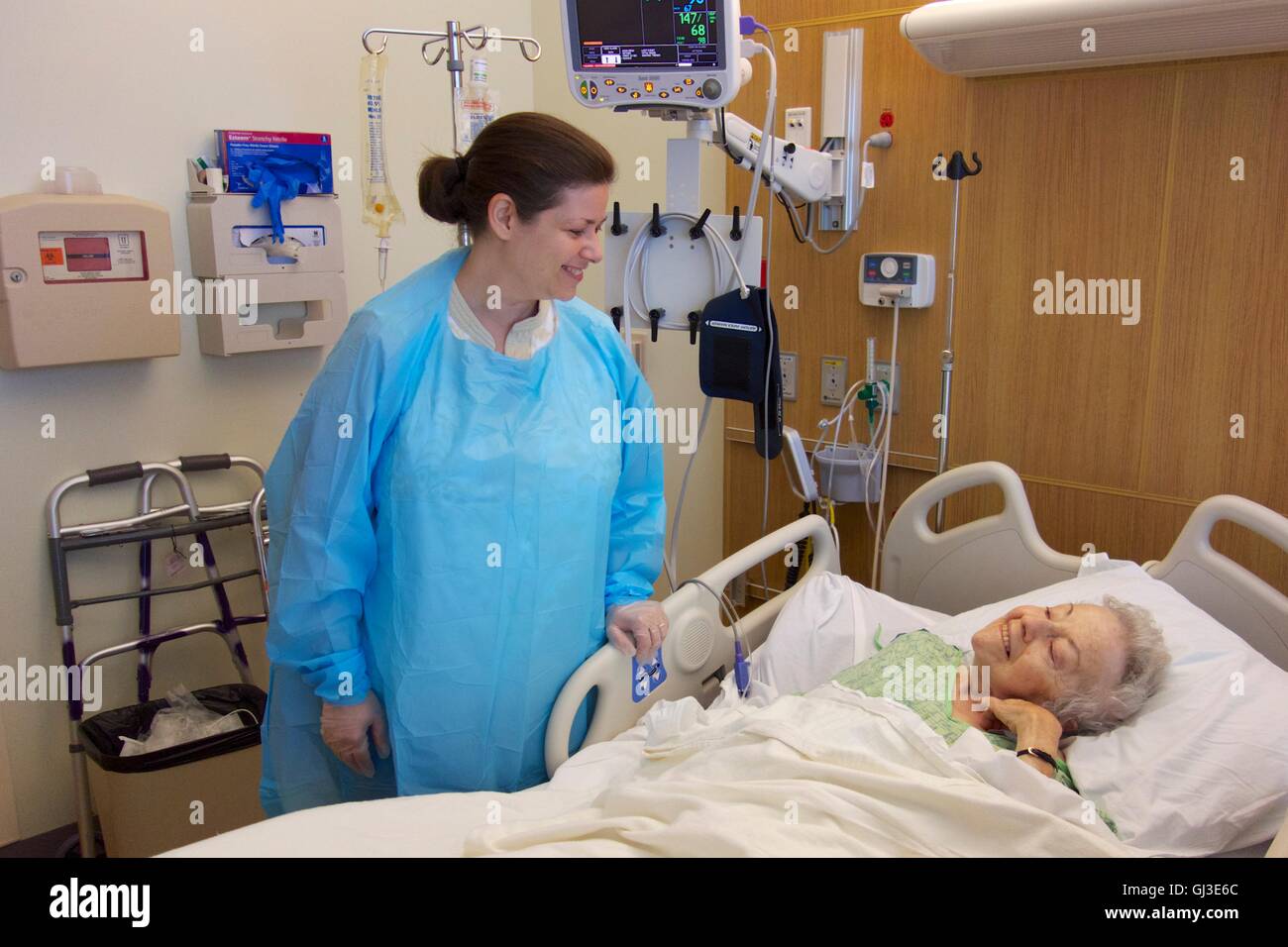 Woman visiting sick grandmother in hospital, wearing gown and gloves due to Clostridium difficile infection in older woman. Stock Photo