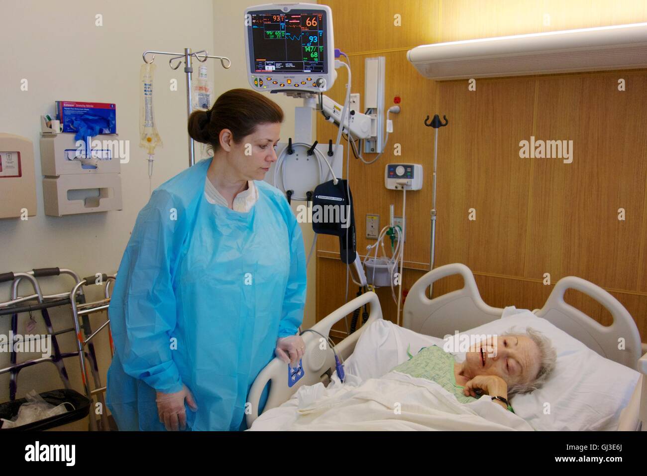 Woman visiting sick grandmother in hospital, wearing gown and gloves due to Clostridium difficile infection in older woman. Stock Photo