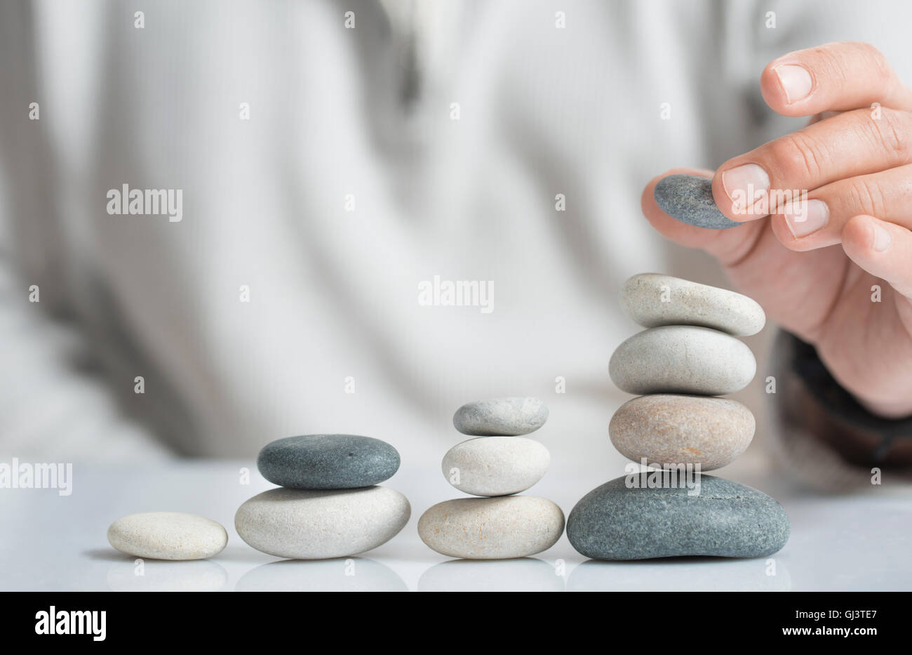 Horizontal image of a man stacking pebbles on a table with copyspace for text. Concept of risk management and wealth. Stock Photo