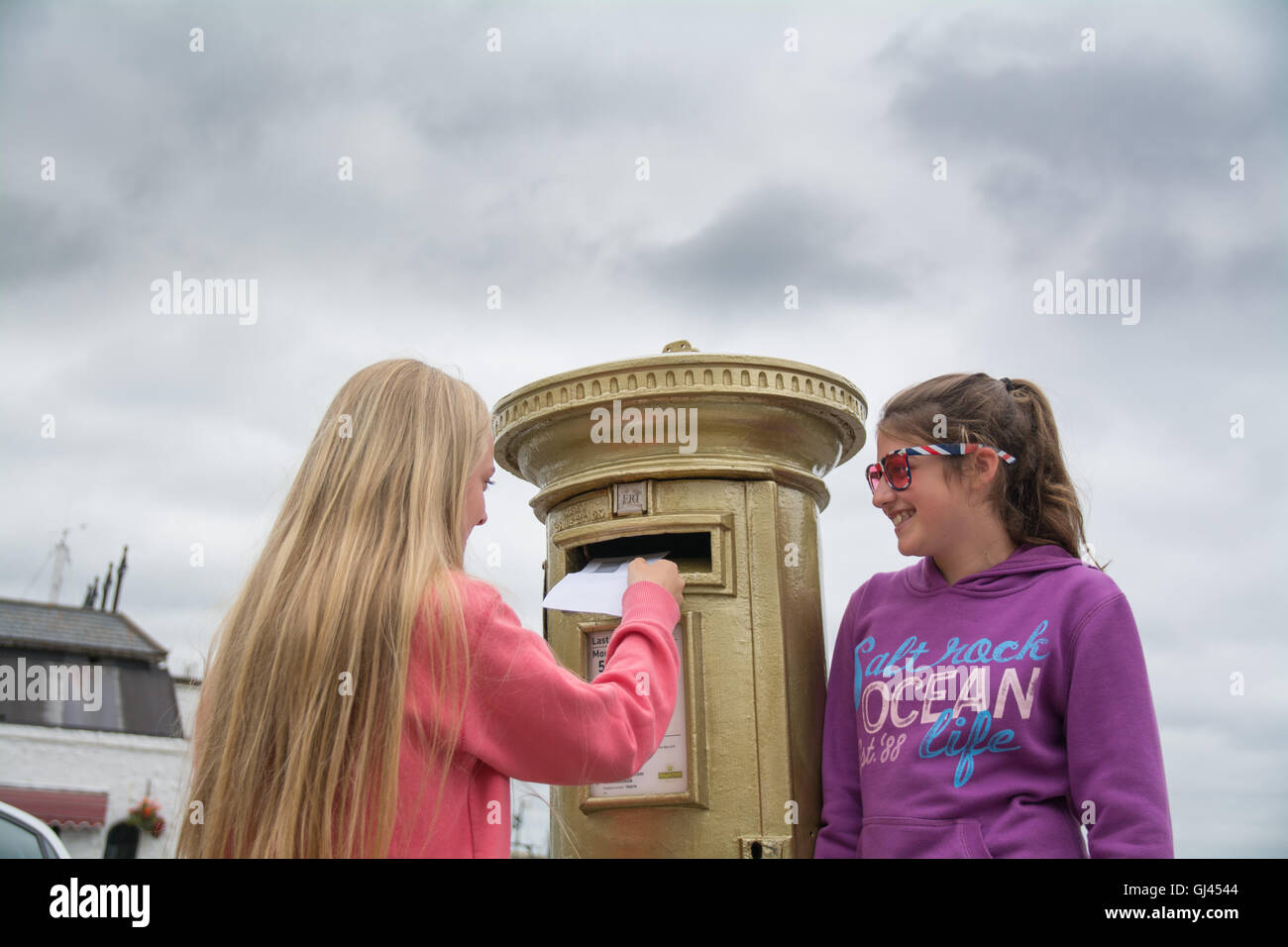 Penzance, Cornwall, UK. 12th August 2016.  The golden postbox in Penzance in honour of Helen Glover winning gold in the 2012 Olympics. Helen is due to race in the Coxless pairs with Heather Stanning at Rio, and are going for gold again ! Seen here Kitty and Lana Credit:  Simon Maycock/Alamy Live News Stock Photo