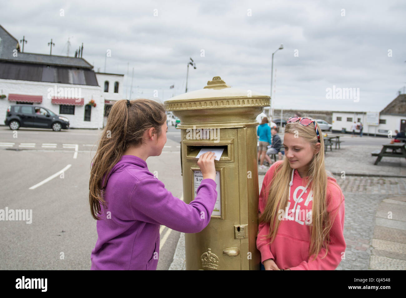 Penzance, Cornwall, UK. 12th August 2016.  The golden postbox in Penzance in honour of Helen Glover winning gold in the 2012 Olympics. Helen is due to race in the Coxless pairs with Heather Stanning at Rio, and are going for gold again ! Seen here Kitty and Lana Credit:  Simon Maycock/Alamy Live News Stock Photo