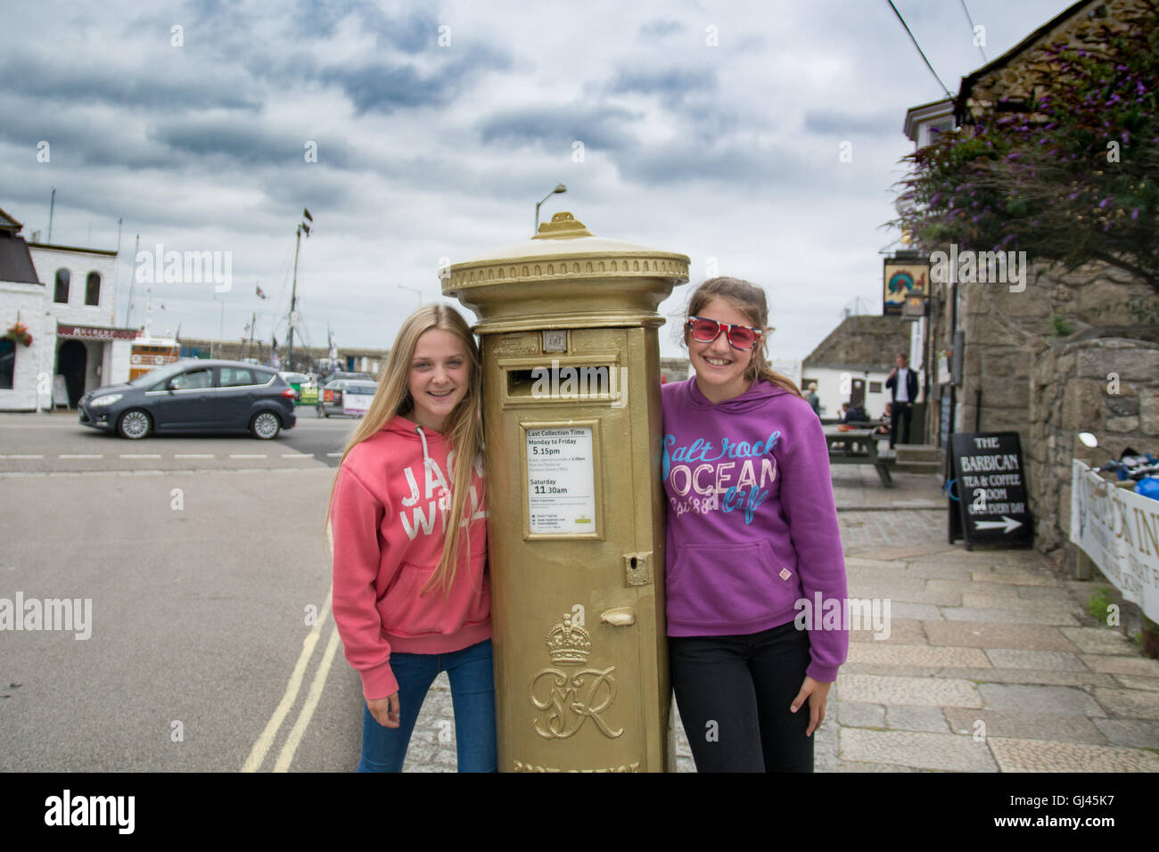 Penzance, Cornwall, UK. 12th August 2016.  The golden postbox in Penzance in honour of Helen Glover winning gold in the 2012 Olympics.Helen and her partner  Heather Stanning have successfully defended their title winning another gold medal.  Seen here Kitty and Lana Credit: © Simon Maycock/Alamy Live News  Stock Photo