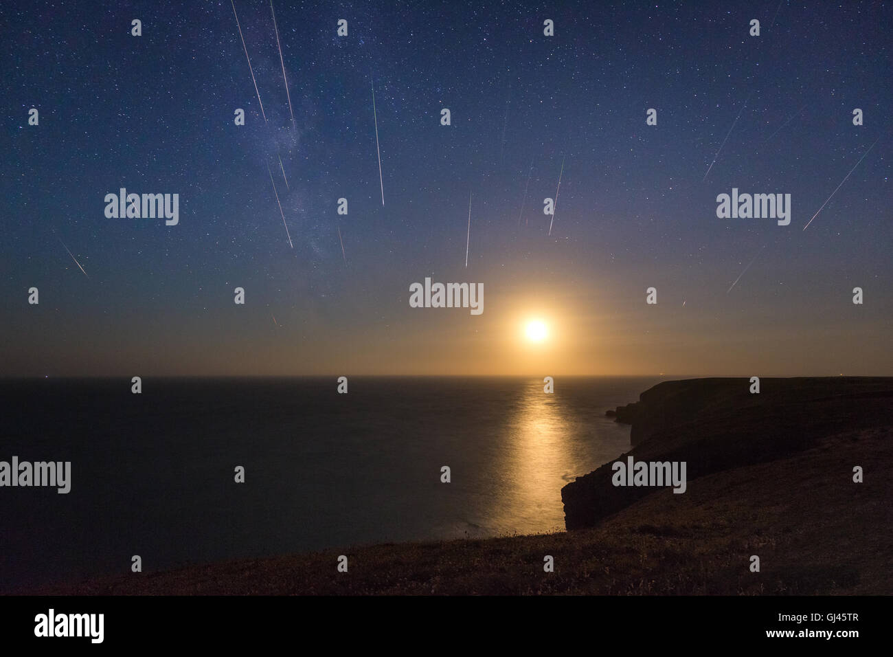 Pembrokeshire, Wales, UK. 12th August, 2016. The setting moon reflected in the sea on the Pembrokeshire coastline in Wales, pictured is a compilation of an hour worth of meteors from the Perseid Meteor shower Stock Photo