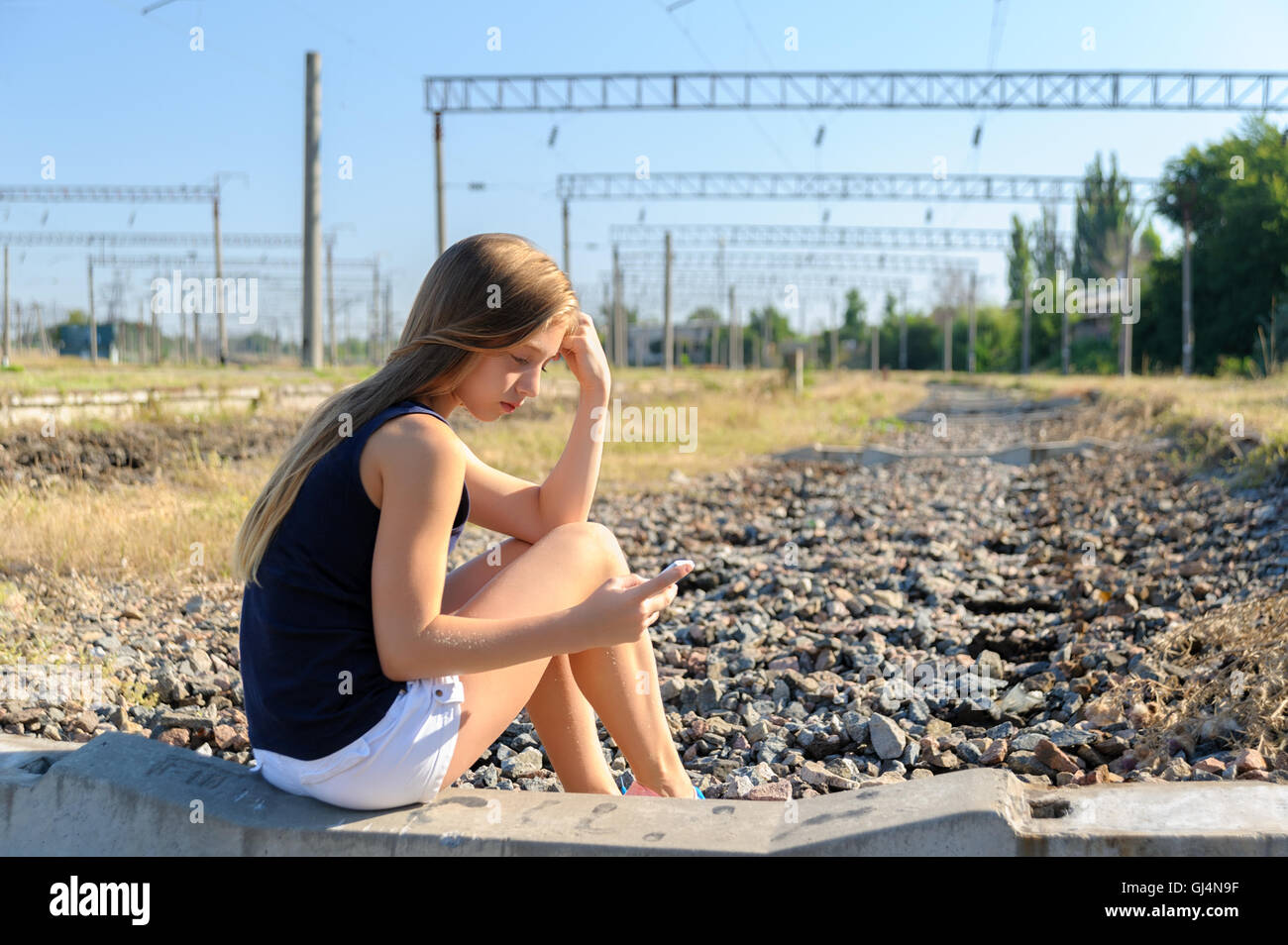 Teenager girl with mobile sitting on unfinished rail track Stock Photo