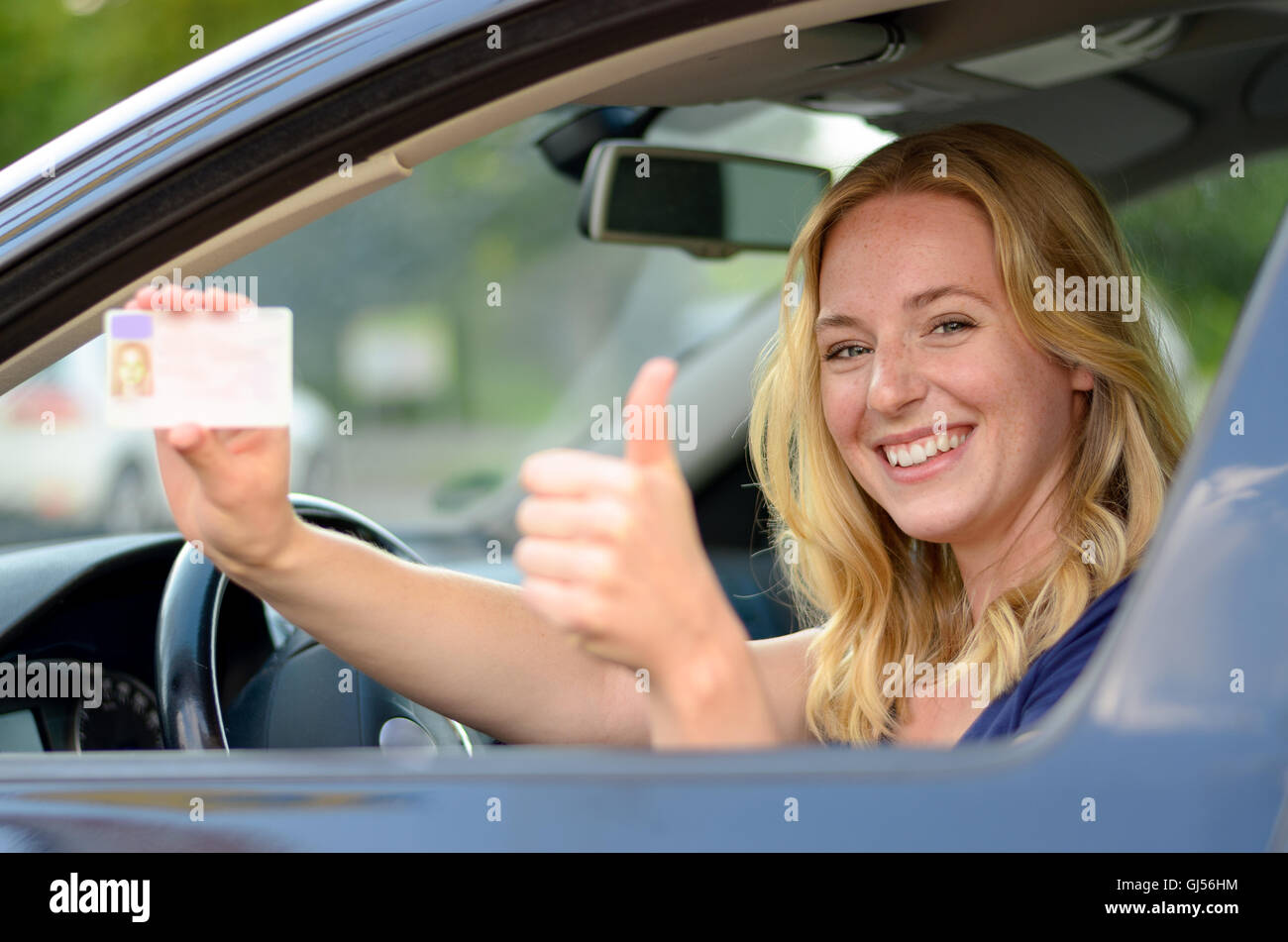 Young blond woman sitting behind the steering wheel of a car showing
