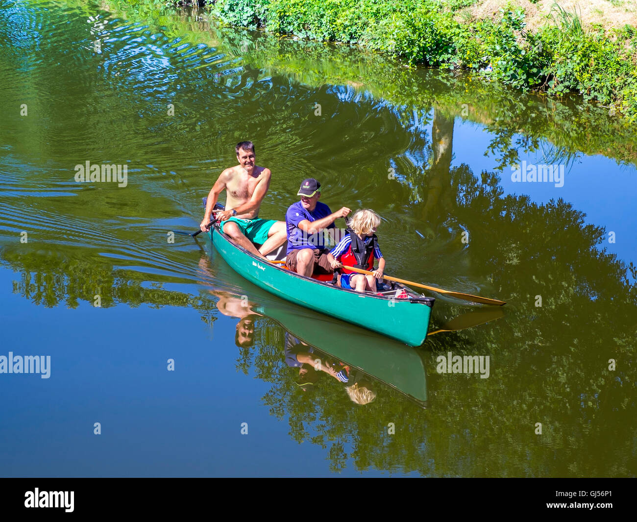 Two men and child paddling canoe on river - France. Stock Photo